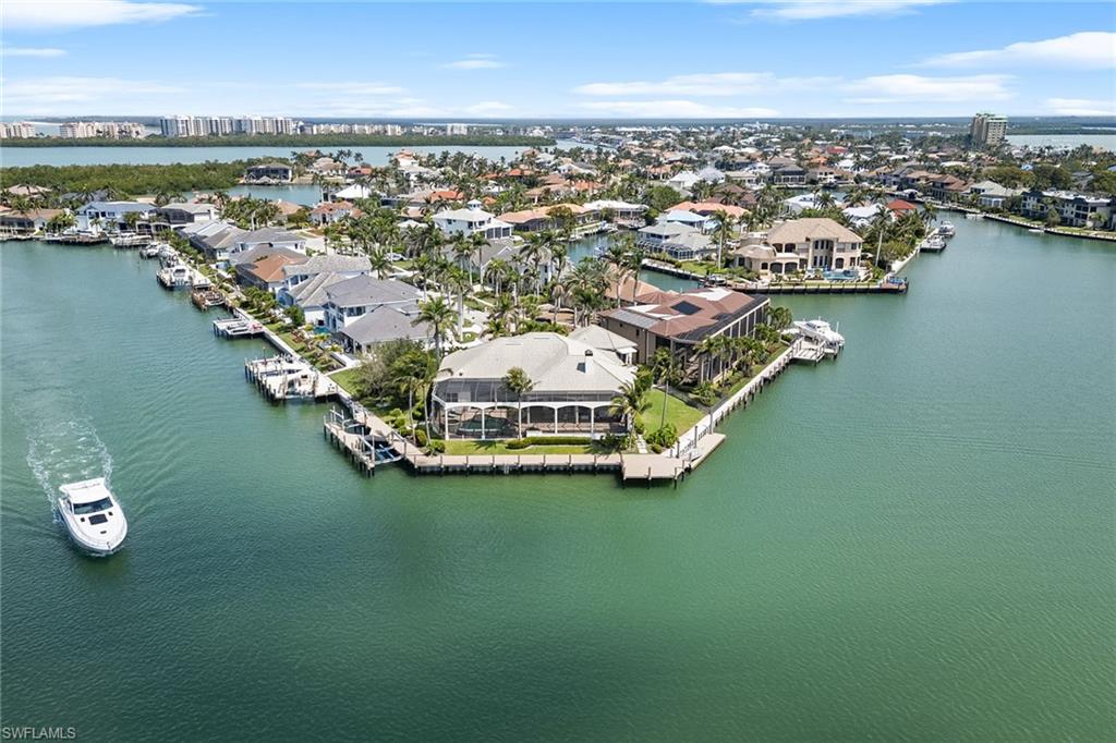 Rarely available, this gorgeous estate on Smokehouse Bay offers over 250 feet of water frontage on a pie-shaped lot with southern exposure, providing spectacular sunsets and views. At the end of a quiet cul-de-sac, this six-bedroom plus den, four-and-a-half-bath home offers quick, direct Gulf access and a premier waterfront lifestyle. The property boasts three private docks, one equipped with dual boat lifts (12,000- and 20,000-pound capacity), a second fixed dock and a third 50-foot floating dock. The seawall and all docks are just two years old. Inside, refined architectural details include volume ceilings, crown molding and custom ceiling treatments. Tile in the main living areas and warm wood flooring in the bedrooms and den create a cohesive, elegant look. The chef's kitchen is a showstopper with quartz countertops, a tile backsplash, under-cabinet lighting, appliances including a six-burner gas range with pot filler and hood, two paneled dishwashers, and a paneled refrigerator-freezer. A center island with a secondary sink and a built-in desk completes the space. The kitchen nook flows into the great room with a custom stone wall, fireplace and built-in entertainment center. Pocketing and zero-corner glass sliders open to the lanai, creating effortless indoor-outdoor flow with breathtaking water views. A formal dining room offers custom lighting, garden-facing windows and built-in cabinetry, while a nearby wet bar with wine refrigerator and shelving elevates the home's entertaining appeal. The living room showcases expansive panorama windows that frame the bay and fill the space with natural light. The owner's suite is a luxurious retreat with French door access to the lanai, wide-water views, a sitting area and two custom walk-in closets with built-ins, one featuring a dedicated washer and dryer. The en-suite bath features dual vanities, a makeup counter, jetted soaking tub and a large, doorless walk-in shower with multiple showerheads. Three guest bedrooms on the main level all enjoy water views. Two share a Jack and Jill bath with dual sinks and a shower-tub combo, while the third offers lanai access and an en suite with walk-in shower. Upstairs, a private guest wing functions like a studio apartment with a kitchenette, private lanai with water views and two bedrooms, one with walk-in closet and custom wall trim, and plantation shutters throughout. The den serves as an ideal office or study, featuring grass cloth wallpaper, custom desk and built-in cabinetry. The air-conditioned tandem garage accommodates three cars and features epoxy flooring and a split air-conditioning system. Outdoors, a screened lanai with travertine flooring is designed for entertaining, featuring a built-in outdoor kitchen, shower, remote-controlled retractable awning and pool bath. The heated infinity-edge pool/spa overlooks water vistas, offering a resort-style retreat. Enjoy the island lifestyle just minutes from award-winning beaches, dining and shopping.