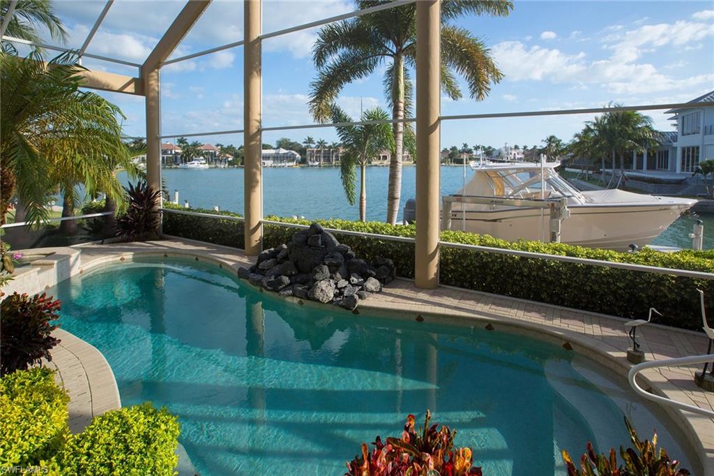 Experience spectacular waterfront views from this amazing direct access custom home with 6053 sq. ft. under air with fireplace in the main living area and tray ceilings in living areas and master bedroom. Just some of the custom features include tile on the diagonal, designer ceiling treatments, columns, archways, faux finishes, wrought iron details, custom built ins, coffered and barrel ceilings, wainscoting and much more. The open kitchen features gorgeous cabinetry, light granite with matching island, Thermador double ovens & gas cook top. The impressive master bath includes Roman columns and soaking tub. Amazing wood paneled den. Waterfront deck adjacent to the PVC dock and lift, plus jet ski lift & outdoor sitting area. This home offers a tropical lanai with pool & spa with natural rock waterfall feature and full outdoor kitchen, with spacious sitting area and additional outdoor seating area.  Upstairs loft area boasts full size bar & balcony overlooking pool and water view. All set in a magnificent landscaped lot immaculately maintained. Additional expansive below house storage area accessible from both the inside and outside via garage door.