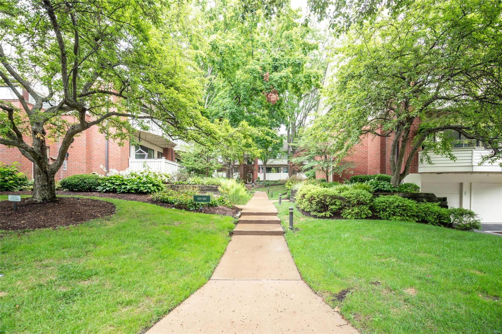 This charming 1st floor condo has it all! The beautiful and lush landscaping is very inviting and this condo is tucked away off Waterman which makes it feel more private. The open concept living room and dining room is very inviting with a wood burning fireplace for those St. Louis winter nights. Hardwood floors and a great porch/ deck perfect for a morning cup of coffee or a nice BBQ.
The kitchen has amble cabinet space and a stainless steel refrigerator and dishwasher. A very nice sized primary bedroom with ensuite and walk in closet is a plus. The 2nd bedroom or office is the perfect size with a full bathroom accessible for guests or from the hall.  Full size washer/ dryer in the 2nd bathroom. Tandem garage parking and large storage in the basement. Easy access to the Central West End/ Kingshighway and Barnes hospital as well as HWY 64. Also close to Washington University and Forest Park. Great walking neighborhood. Location: Ground Level, Interior Unit