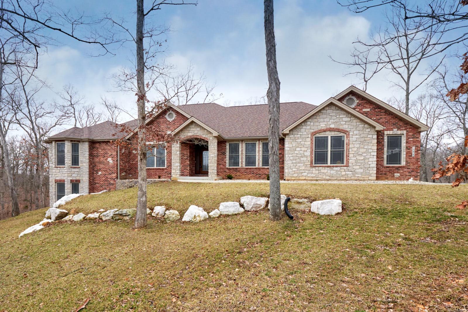Architecturally-appealing exterior w/multiple roof lines, brick/stone facade & three-car side-entry garage. Luxury abounds starting w/the attractive front door & HW floors thru-out the main floor living space. Home office features glass French doors for privacy, built-in desk, cabinets & shelving. Spacious DR is surrounded by stunning coffered ceiling & beautiful archways. Open floor plan encompasses gourmet kitchen (w/stainless appls, stone backsplash, granite counters & huge center island/breakfast bar), breakfast room (w/sliding glass door to covered patio) & roomy, yet cozy great room w/floor-ceiling stone FP & built-ins. Peaceful surroundings of nature can be viewed from the wall of windows & covered patio. Master suite w/coffered ceiling, private door to patio & luxurious bath w/all the bells & whistles. Second & third bedrooms provide a popular Jack/Jill style bath. Walk-out LL is fin. w/huge entertaining area featuring a gorgeous wet bar, two additional bedrooms & full bath.