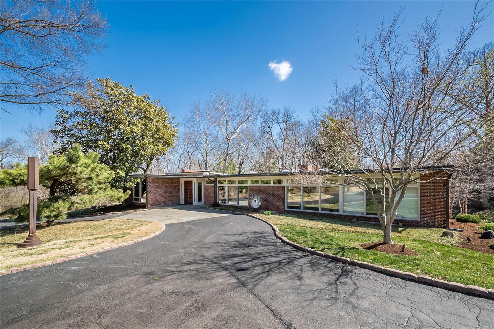 Tucked away on one of Ladue's most desirable lanes, this Benjamin Shapiro-designed mid-century modern home sits on nearly 4 acres of private, park-like grounds. The home welcomes you with a gallery-style entry with floor-to-ceiling windows that flood the home with natural light, showcasing tall ceilings, exposed brick walls, and slate floors. The formal living room boasts 10-foot ceilings and a WB fireplace, while the spacious family room features 12-foot vaulted beamed ceiling, fireplace, built-in bookcases and wet bar with access to the terrace. A gracious dining room and well-appointed eat-in kitchen make entertaining effortless. The main level offers four bedrooms, including a private primary suite with serene views, 2 bedrooms share a bath and one en suite. The lower level includes a large recreation room and guest suite. A three-car garage, amazing closets and storage.  An incredible lot provides privacy-all just minutes from Ladue's best dining, shopping, and top-rated schools.