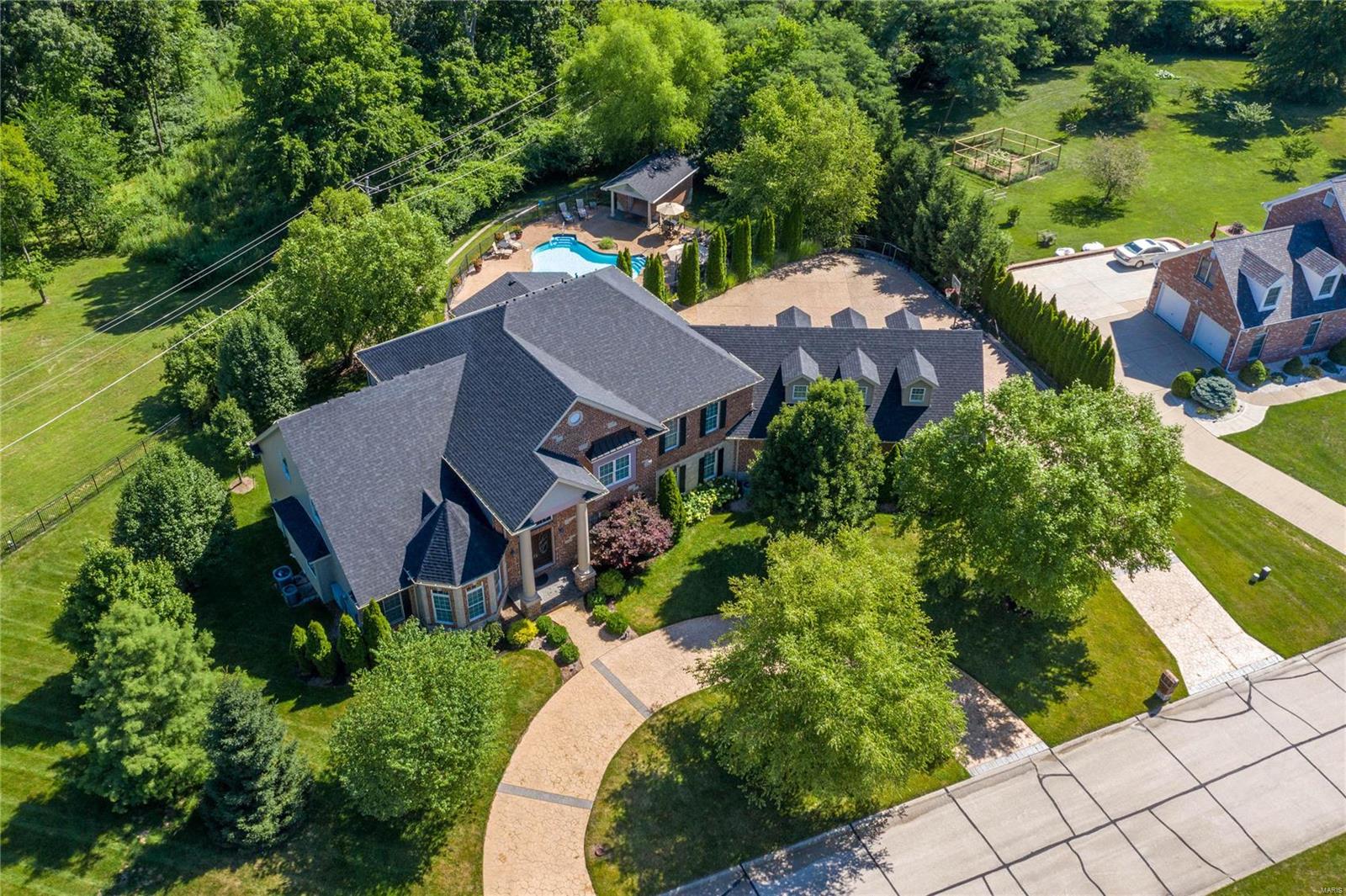 Spectacular brick & stone-crafted Estate home in beautiful Camelot! Impressive 2-sty foyer opens to private study with groin vault ceiling, coffered dining room & 2-sty great room with cast stone fireplace, built-in bookcases & expansive wall of windows. Designer kitchen with granite countertops, glazed cherry cabinetry, commercial grade appliances & 10’ center island adjoins light-filled breakfast room with sliding glass door to veranda & hearth room highlighted by fireplace. The master bedroom suite offers an appealing retreat with wide bay window & lavish bath with jetted tub & shower spa. The 2nd floor extends the living quarters with 3 additional bedrooms, 2 with ensuite baths, & hall full bath plus bonus loft room & family room with built-in work center. Lower Level includes recreation room with floor-to-ceiling fireplace, game room, dining area, workout room, 5th bedroom & full bath. Situated on a 1-acre lot with resort style pool, pool house & 4-car garage with guest quarters.