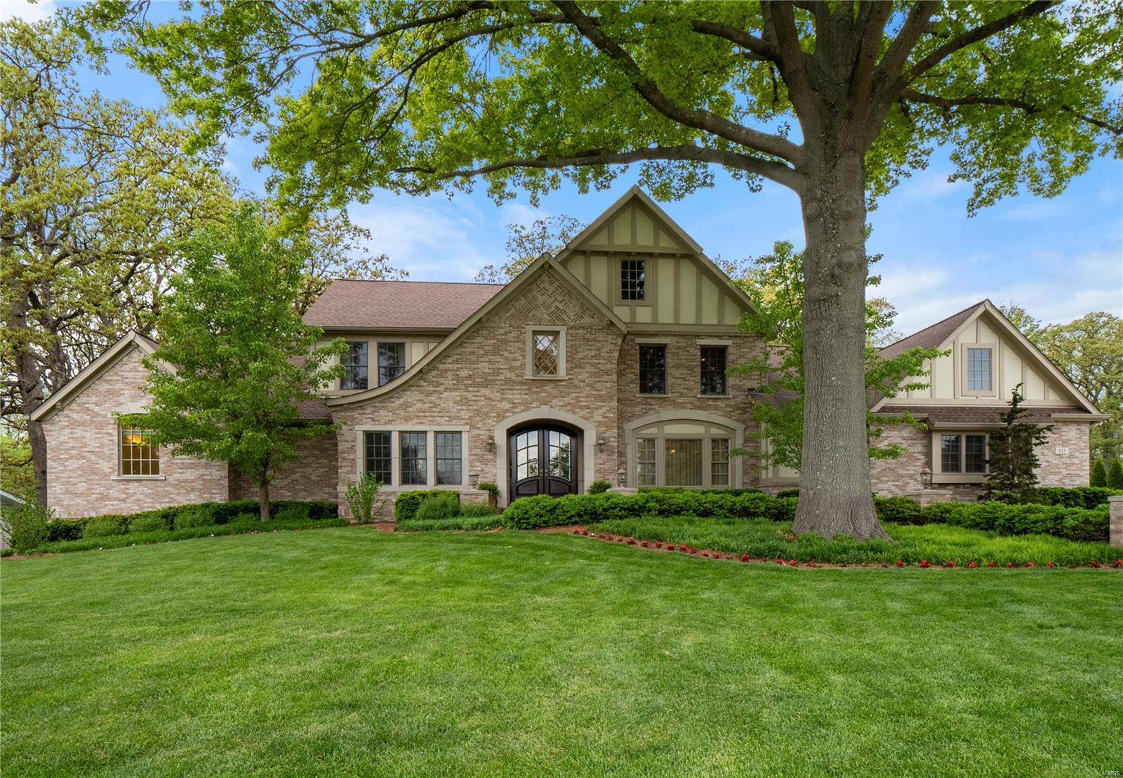 Exceptionally built & intentionally designed with the highest quality finishes. This newer 1.5 story Tudor sits quietly back on an acre lot within the Ladue School District. Take in the lush landscape of the private backyard from the stone clad patio w/ fireplace, built-in grill & green egg smoker. Adorning the main level are beautifully refinished 5’’ plank wood floors, crown moldings & high ceilings. A grand 2-Story great room is fit w/ gas fireplace, built-in shelves & fully-equipped wet bar. The high end kitchen opens to a sunken hearth rm w/ wood beamed vaulted ceilings & stone fireplace. A main floor master provides fine luxuries: travertine stone, double vanity, Airjet tub, his/her closets & laundry area. Upstairs are 3 ensuite Bdrms all w/ walk-ins & a hall laundry. An entertainer's dream, the knockout LL transports you to an Irish pub: 9-seat bar w/ built-in banquette, billiards space, media area, 5th bedroom/exercise, full bth & a mini astroturf soccer field! MUST SEE!