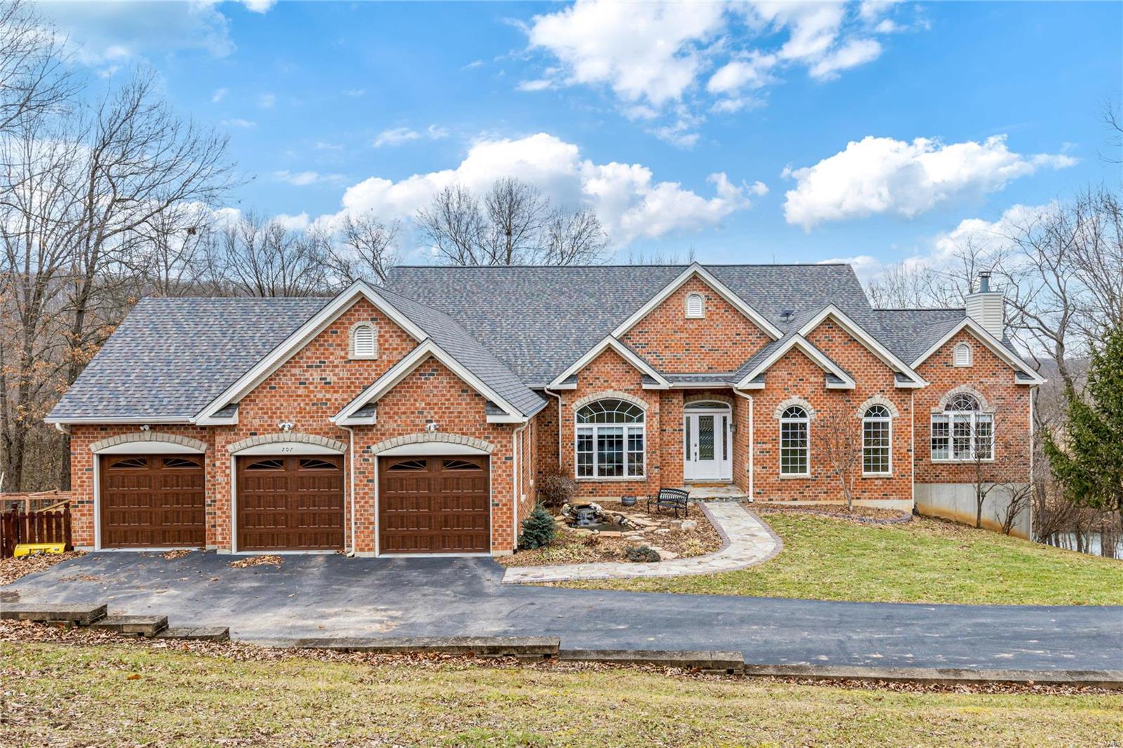 Overlooking the golf course, this spectacular brick & stone great room ranch sits on wooded 3+- ac grounds in Paradise Valley's gated community. Open floor plan features Brazilian walnut hardwoods, 12’ ceilings, detailed trim work & serene views of the natural surroundings from expansive windows. Granite foyer leads to formal dining room & vaulted great room highlighted by floor-to-ceiling Auxvasse stone fireplace. Designer kitchen featuring quartz counters, 42” maple cabinetry, Café appliances & 8’ island with waterfall edges adjoins breakfast room with adjacent screened porch & hearth room with wet bar & stacked stone fireplace. Primary suite with direct vent fireplace & luxury bath with shower spa & bubble jet tub plus 2 add'l bedrooms & hall full bath complete the main floor living quarters. Lower Level includes rec room with fireplace, wet bar, 2 ensuite bedrooms & walks out to the outdoor living area with covered & open decks featuring new TimberTech decking & hot tub patio.
