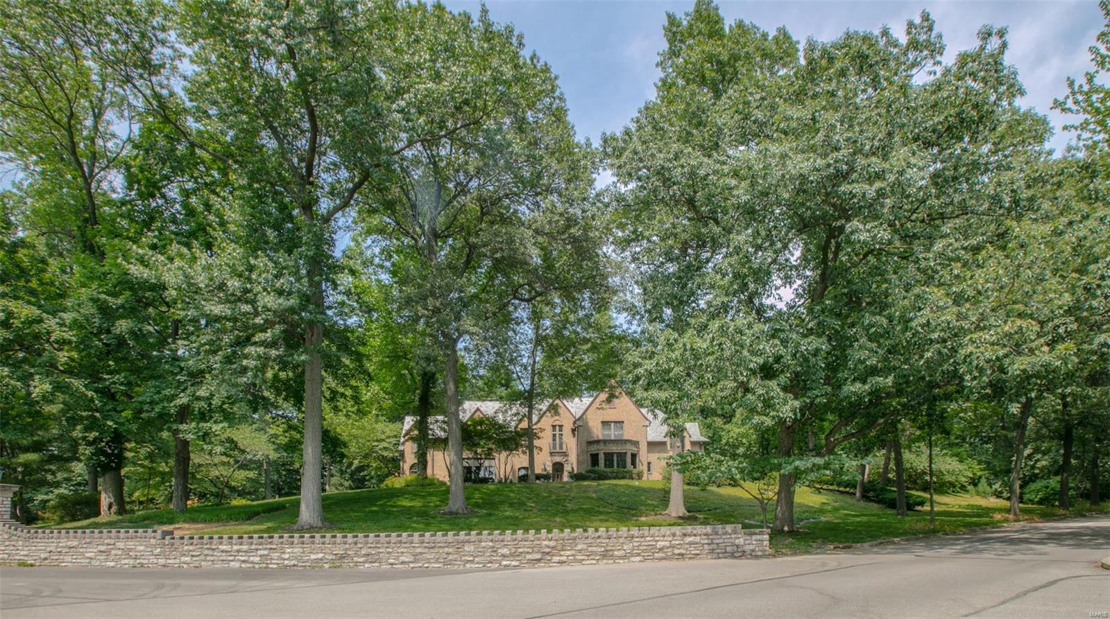 The glamor of old Hollywood resonates within this substantial Tudor home perched above Wydown Boulevard at Clayton’s most prestigious address! Make a dramatic entrance through the elegant foyer with a stunning curved staircase into a gracious sunken living room with an Italian imported stone fireplace and warm wood ceiling. French doors open to a sunroom with unique antique door ceiling. The spacious dining room is outfitted in breathtaking original millwork. Side-by-side kitchen and family room could be combined to elevate this home to 21st century lifestyles. The second floor has a romantic master suite with spaces to create your dream ensuite plus five additional bedrooms, one of which could potentially make a perfect laundry room. Historically significant and lovingly cared for over the past 50 years by the same owner, architectural details abound at Number One Carrswold Drive! Six bedrooms, four and a half baths in 5,253 square feet on over an acre of land, ready for your updates! Additional Rooms: Sun Room