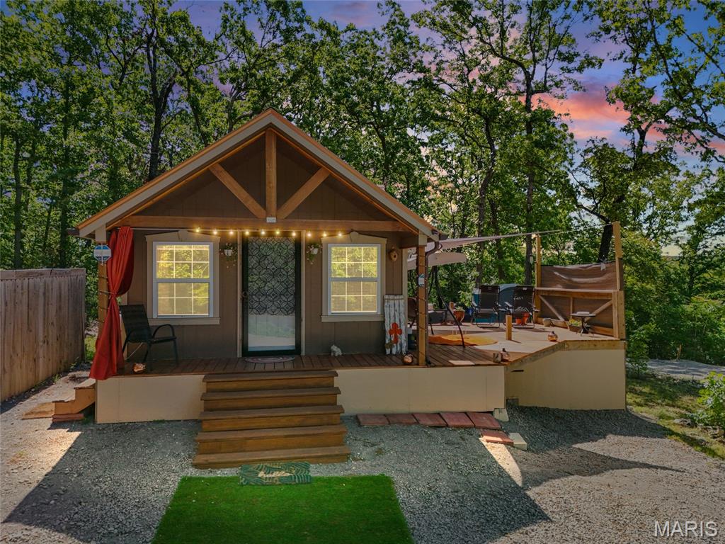 Some decisions are easy - this is one of them. This cabin at Goose Creek is worth a serious look. 600SF of well-designed main-floor living, a 50-square-foot lofted bedroom tucked above, 1 full bathroom, and a lakefront community surrounding all of it. Set on a partially wooded lot, the cabin opens onto a wraparound front porch that sets the tone before you even step inside. Morning coffee, evening cocktails, rainstorms watched from a dry chair — you'll use it in every season. Inside, the craftsmanship is immediately apparent. Custom tongue-and-groove vaulted wood ceilings make the 600-square-foot footprint feel considerably larger than it measures, and hardwood flooring runs throughout the main level. Recessed lighting keeps the space bright and modern. The loft bedroom above has a cozy, treehouse quality — a sleeping space guests will fight over. The cabin handles winter just as well as summer. A mini-split system for heating/cooling means year-round comfort and low energy bills. Upgraded insulation keeps the space practical and efficient through Missouri's colder months. A durable metal roof and T1-11 wood siding keep exterior maintenance minimal. An instant hot water heater and stackable washer/dryer round out a cabin that was clearly designed for someone who actually planned to live here.  A 600-gallon water catchment system serves the sinks, soaking tub, toilet, and washing machine. The side deck and private patio extend things outdoors, where you can truly relax. Goose Creek is a gated lakefront community centered on a 400-acre spring-fed lake. Boating, swimming, and fishing are all waiting for you - and a private beach, pool, recreation center, stocked fishing ponds, and playground give residents a range of amenities that serve every age and pace. Secure key card entry with 24/7 guard service means your property is secure whether you're in residence or away. This property is offered as-is and is in exceptional condition (built in 2022). It's move-in-ready with solid bones, quality finishes, and a community that delivers on the promise of lake life year-round. Come see it before someone else does.