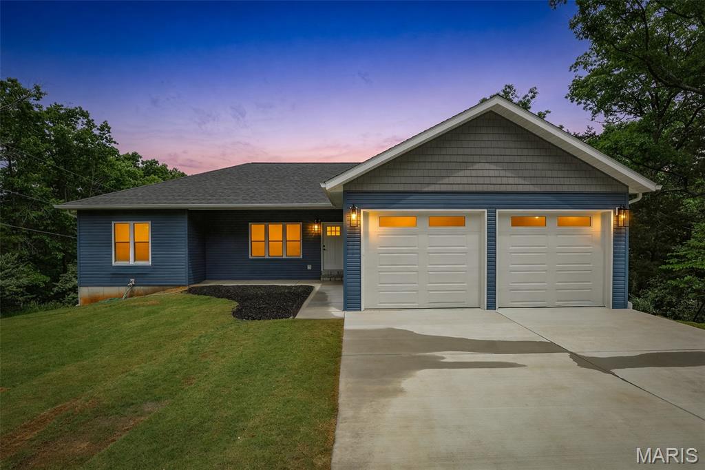 This stunning new-construction home showcases top-notch craftsmanship throughout, offering 3 bedrooms, 2 baths, and approx. 1,600 sq ft of beautifully designed living space. The home features both an open-concept main living area and a split-bedroom layout, giving buyers the best of both worlds—spacious gathering areas plus privacy for the bedrooms.  The living room includes a cozy propane fireplace and durable luxury vinyl planking flooring that flows through the main areas. The kitchen stands out with custom soft-close cabinetry, dovetail drawers, stylish two-tone design, quartz countertops, a center island, breakfast bar seating, and energy-efficient stainless-steel appliances.  The primary suite offers a generous 10x10 walk-in closet and a spa-like bath with double vanity and a large walk-in shower featuring multi-head fixtures. Secondary bedrooms include upgraded carpet and padding for added comfort. A sliding glass door off the dining area leads to a deck overlooking a peaceful wooded backdrop. The full walkout lower level is ready for future finishing and includes a rough-in for a full bath. Outside, enjoy a backyard patio and a freshly installed Bermuda baseball-grade sod lawn, giving new owners an instant, lush yard. The home also includes an oversized 2-car garage with smart garage doors for added convenience.  Located in the desirable Terre Du Lac lake community, residents enjoy access to 16 lakes, beaches, golf courses, parks, and year-round recreation. This home blends quality construction with the relaxed lake-community lifestyle buyers are seeking.