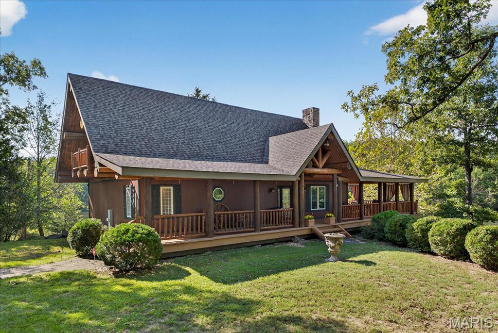 At the end of a quiet drive—just beyond the flurry of St. Louis—a story begins to unfold. Set across 40 acres of unspoiled landscape, this remarkable log home offers more than a residence; it is a way of life defined by calm, connection, and natural beauty. As you arrive, the land opens gently to reveal a private 5-acre lake, its still waters reflecting the surrounding woods and sky. The home is thoughtfully positioned to take full advantage of these views, with a lakeside dock and patio inviting slow mornings, quiet afternoons, and evenings spent watching the light fade across the water. Inside, the great room immediately draws you in—a soaring space framed by warm knotty pine ceilings and anchored by a striking 21-foot stone fireplace. Morning begins in the kitchen, where sunlight filters through the trees and settles across warm wood cabinetry. Coffee lingers a little longer here with flowing conversations around the central island as the day gently takes shape. From there, the home opens effortlessly between the kitchen, dining, and living spaces, where the atmosphere remains deeply inviting.?? A haven for relaxation, the main-level primary suite showcases a beautifully renovated bath with dual vanities, a linen closet, soaking tub, and an expansive shower, while a generously sized walk-in closet completes the space, offering everyday convenience. The upper level features a lofted area—ideal for casual games or a quiet reading nook—as well as two bedrooms that share a bath and a balcony with scenic views of the property. The walk-out lower level extends the home’s versatility, with a fourth bedroom, full bath, recreation space, laundry, substantial storage, and a dedicated workshop—ideal for hobbies or projects. Outdoors, a wraparound covered porch, expansive deck, and shaded patio create cohesive spaces to gather, entertain, or simply take in the quiet beauty of the setting. A second pond, along with a metal barn and additional lean-to, enhances the property’s functionality for equipment, animals, or activities. Meticulously maintained and smartly equipped with geothermal heating and cooling, a whole-house water softener, central vacuum, and camera-monitored security, the home balances rustic character with modern convenience. Accessed by a well-kept private road and located just over an hour from St. Louis, this is more than a getaway—it’s a place to slow down, reconnect, and experience the beauty of each season in a setting that feels worlds away.