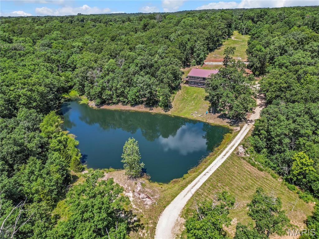 Escape to your own private retreat on 25 beautiful wooded acres, abundant with wildlife and featuring a picturesque one-acre stocked lake. Lovingly enjoyed by the current owners for many years, this property is ready for its next chapter and new memories to be made. The spacious 3-bedroom, 3-bath home offers additional sleeping rooms and a versatile layout that could easily accommodate separate upper and lower-level living quarters. Whether you're looking for a mother-in-law suite, multi-generational living, or a property to share with family, the possibilities are endless. The low-maintenance exterior features vinyl siding and a metal roof, while the wraparound porch provides the perfect place to relax and take in the peaceful surroundings from every angle. Inside, the main level showcases a beautiful open floor plan designed for gathering, allowing everyone to stay connected whether cooking in the kitchen or relaxing in the living area. The main-floor master suite offers convenience with its private bath, walk-in closet, and laundry area, while an additional office or nursery provides extra flexibility. The lower level is equally impressive, featuring its own living room and dining area, two bedrooms, an additional sleeping room, and a hobby room. A kitchen could easily be added back to complete a second independent living space. Throughout the home, common areas have been thoughtfully designed to capture beautiful lake views. Completing the property is a well-built 30'x40' metal shop with a concrete floor and office space inside, perfect for storing ATVs, equipment, and everything needed to enjoy and maintain this incredible acreage. If you've been searching for privacy, recreation, and a home that offers room for everyone, this one-of-a-kind property deserves a closer look.