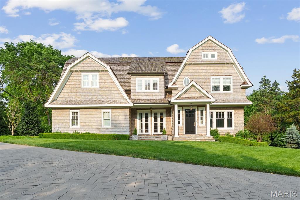 Step into timeless elegance with this stunning Cape Cod Shingle-style home, crafted with precision and sophistication by Slavin Homes. Nestled in the prestigious community of Ladue, this exceptional residence boasts architectural beauty, meticulous detail, and refined craftsmanship throughout.
As you enter the paneled foyer, you are greeted with custom touches that set the tone for the home's exquisite interior. The gracious floorplan seamlessly blends traditional charm with modern luxury, offering an inviting atmosphere for both grand entertaining and intimate gatherings. The main-floor primary ensuite is a true sanctuary, featuring spa-like amenities and opening to a heated covered patio through two sets of elegant French doors. This seamless indoor-outdoor connection provides year-round enjoyment, perfect for morning coffee or evening relaxation. The heart of the home is its oversized custom kitchen, meticulously designed for culinary excellence. The expansive great room is an entertainer’s dream, complemented by designer lighting, exquisite wallcoverings, and bespoke fixtures that add warmth and sophistication. Upstairs enjoy another primary ensuite, and two additional bedrooms and bathrooms, plus a bonus room. The lower level includes a family room, luxurious custom bar, and gym. Outside, a stunning pool, manicured grounds, pool house, and outdoor kitchen awaits—boasting unparalleled beauty and distinction.