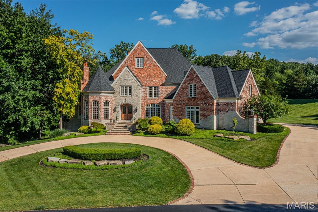 A striking residence defined by timeless architecture, exceptional scale, and a beautifully crafted interior. The dramatic two story foyer welcomes you with a graceful curved staircase and refined millwork, setting the tone for the craftsmanship carried throughout the home. The main level is designed for both elegant entertaining and comfortable daily living. The impressive living room showcases soaring beamed ceilings, a dramatic wall of windows that fills the space with natural light, and a stunning floor to ceiling stone gas fireplace that anchors the room. Nearby, the vaulted hearth room offers a warm and inviting gathering space and opens directly to a spacious composite deck overlooking the spectacular pool and natural cascading waterfall. The gourmet kitchen is well appointed with premium appliances including a Wolf six burner gas cooktop and Sub Zero refrigeration. Custom cabinetry and generous preparation space create an exceptional culinary environment, while a secondary staircase nearby provides convenient access to the upper level. The main floor primary suite offers a private retreat with French doors, a beautifully detailed coffered ceiling, a custom dressing room, and direct access to a private study. The bath includes dual marble topped vanities and a spacious shower. Upstairs offers five spacious bedrooms and three well appointed baths. The expansive lower level is designed for recreation and entertaining with a large gathering area, billiards space, fitness room, wine cellar, wet bar, and an additional bedroom suite. A massive theater room creates a true cinematic experience, while extensive built in storage provides exceptional organization. A fourth fireplace anchors the lower level. Significant investment has also been made behind the walls to enhance the home’s essential systems and infrastructure, ensuring long term performance and peace of mind. Outdoors, the property becomes a private wooded retreat featuring a resort style pool with cascading waterfall. Beneath the deck, a rain management system keeps the covered patio dry and comfortable in virtually any weather, creating an inviting outdoor living space throughout the seasons. A rare offering that combines architectural presence, thoughtful improvements, and exceptional amenities.