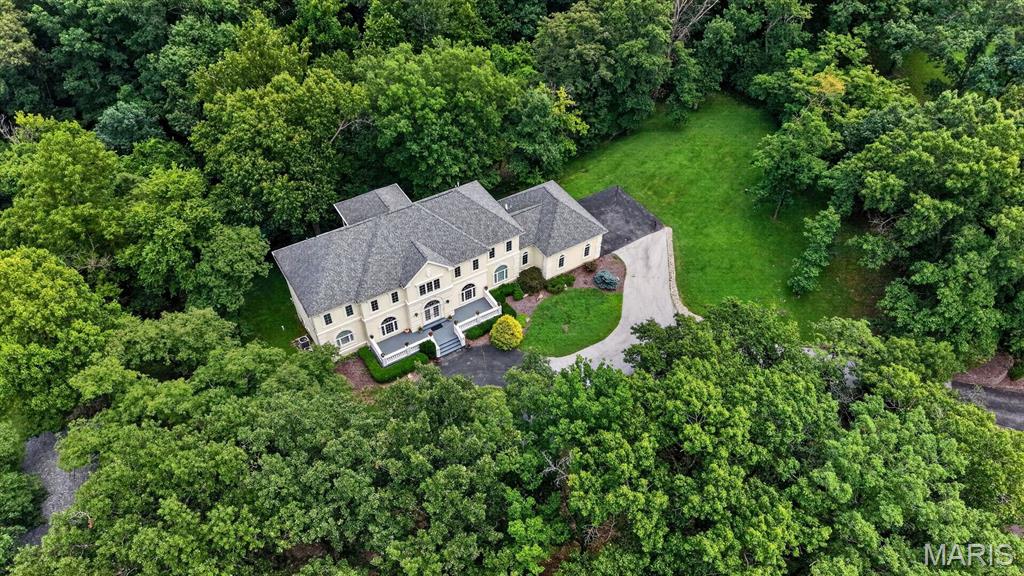 Gracefully perched atop 3.3 private wooded acres in prestigious Chesterfield Lakes, this extraordinary custom estate by acclaimed builder Keith Schroeder offers timeless architecture, refined luxury, and exceptional privacy. A dramatic two-story foyer opens to a spectacular great room with soaring ceilings and a wall of windows framing breathtaking views. Rich millwork and quality craftsmanship are showcased throughout. The gourmet kitchen features premium appliances, custom cabinetry, an expansive center island, and flows seamlessly into the breakfast room and adjoining great room—ideal for everyday living and entertaining. The main-level primary suite is a luxurious retreat with a spa-inspired bath, while a formal dining room, private study, mudroom, and laundry complete the first floor. Upstairs are three spacious bedrooms, two full baths, and a versatile bonus room. The finished walk-out lower level offers a theater room, recreation space, an additional bedroom and bath. A restored 750+ sq. ft. outbuilding, originally the property's historic barn, provides endless possibilities for a studio, workshop, hobby space, or additional storage. An exceptional offering of luxury, privacy, and natural beauty.