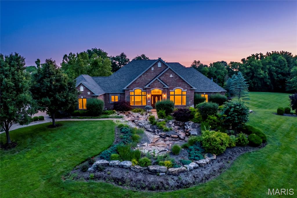 Stunning brick and stone ranch-style home sitting on 3 private acres surrounded by mature trees and scenic views! This custom-built home boasts 5 bedrooms, 4 full bathrooms, 3 half bathrooms, and over 6,500 square feet of living space including the finished walkout lower level. The property also features an attached 3 car garage and a detached 52 x 40 foot detached garage with a bonus room.

The front door opens to the impressive entry foyer with a gallery staircase and leads to the elegant dining room and stunning great room. The great room boasts a floor-to-ceiling brick fireplace, custom millwork, a wall of windows overlooking the grounds, and French doors that open to the expansive deck.

The designer kitchen features custom glazed cabinetry, granite countertops, commercial-grade appliances, a butler’s pantry, dining area with a bay window, and opens to the hearth room with a beautiful brick and stone fireplace. The light-filled sunroom provides the perfect place to relax and enjoy the picturesque setting.

The luxurious main floor primary suite boasts a brick fireplace, private sitting area, deck access, walk-in closets, and a spa-like bathroom with a jetted tub, separate shower, and dual vanities. The stylish powder room and laundry room complete the main level.

The finished walkout lower level is designed for entertaining and features a spacious recreation room with a stone fireplace, wet bar, office, workout room, guest suite, two additional bedrooms connected by a Jack and Jill bathroom, and a half bathroom. The lower level also features ample storage space.

Other highlights include: extensive custom millwork, coffered ceilings, professional landscaping, multiple waterfalls, newer hardwood floors on the main level, and painted neutral colors throughout most of the home.

Relax outside on the expansive deck overlooking the scenic grounds, enjoy the beautifully landscaped yard with waterfalls. Location could not be better – close to major highways, restaurants, shops, parks, hiking trails, wineries, and Francis Howell schools!