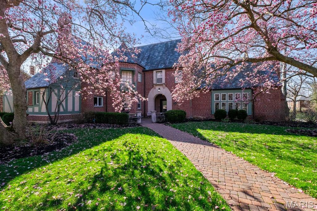 First showings at Open House on Sunday, 4/26 from 1-3pm. Along the iconic, tree lined stretch of Wydown Boulevard, where morning light filters through a canopy of mature trees and daily life unfolds with runners, walkers, and children heading to school, this distinguished Tudor residence introduces itself with quiet presence and enduring character. Set within Claverach Park and moments from Forest Park and the area’s most celebrated dining, the setting reflects a rare balance of energy, tradition, and refinement within the Clayton School District. Inside, a gracious entry with sweeping staircase and terrazzo floors reveals the home’s architectural pedigree. The living room is nothing short of dramatic, with a soaring beamed ceiling rising to nearly twenty feet, leaded glass windows, and a commanding stone fireplace that anchors the space. French doors open to a newly restored covered terrace, offering a natural extension of the interiors. At the heart of the home, the kitchen has been completely reimagined and recently featured in St. Louis Magazine, serving as a true centerpiece. Custom cabinetry, premium appliances, and meticulously curated finishes define the space, while hidden charging stations are seamlessly integrated for modern living. Historic elements, including sandblasted radiator cabinetry, have been thoughtfully preserved and reinterpreted. A refined palette complements the natural wood tones and terrazzo, while architectural ceiling detail and abundant natural light elevate both form and function, creating an environment equally suited for daily living and sophisticated entertaining.The dining room retains its original chandelier and sconces, offering a sense of timeless elegance with French doors that extend gatherings outdoors. The primary suite provides a serene retreat with generous closets and a beautifully appointed bath featuring dual vanities, a soaking tub, and a separate shower. Three additional bedrooms and two well appointed baths complete the upper level. The lower level offers flexible recreation and storage. As the home unfolds outward, its scale becomes even more compelling. Set on approximately three quarters of an acre, the grounds offer a rare sense of space and possibility, equally suited for quiet enjoyment or future vision. A gated drive leads to a two car garage with additional covered parking, reinforcing both privacy and convenience. Extensive improvements including full electrical replacement, new HVAC systems, slate roof updates, and historically appropriate tuck pointing ensure the integrity of the home for years to come.This is a property where architecture, setting, and lifestyle align, offering a timeless residence in one of Clayton's most storied and beautiful neighborhoods.