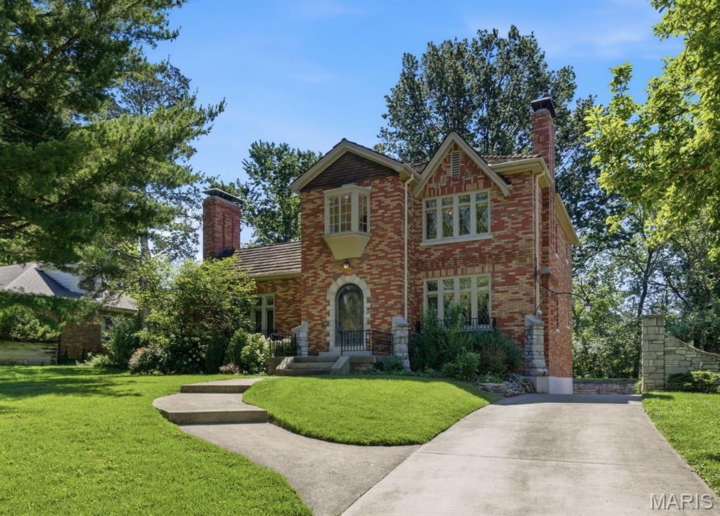 Nestled on more than .6 acres in the prestigious community of Grantwood Village, this distinctive 4-bedroom, 3-bath home offers nearly 2,800 square feet of timeless character, generous living spaces, and endless potential. Surrounded by mature trees on a picturesque lot, this is a rare opportunity to own a home with architectural details that simply can’t be replicated today. Step inside to an impressive vaulted living room where soaring ceilings, a dramatic staircase balcony, beautiful stained glass windows, and an ornate fireplace create an unforgettable first impression. The adjoining sunroom is wrapped in oversized windows, flooding the space with natural light while providing peaceful views of the expansive backyard throughout every season. The charming kitchen features a built-in breakfast nook, creating the perfect spot to enjoy your morning coffee while overlooking the surrounding landscape. A main-floor bedroom and full bath provide flexibility for guests, multi-generational living, or a home office. Upstairs, you’ll find three additional bedrooms, including a spacious primary suite featuring double-door closets and a classic oriel window with built-in cabinetry, adding both charm and functionality. All three bathrooms retain their original vintage character, offering timeless style and an opportunity to preserve or personalize. The finished lower level expands your living space with a welcoming recreation room centered around a second fireplace, abundant storage, and convenient access to the attached two-car garage. Combining remarkable architecture, mature grounds, and an exceptional Grantwood Village location, this home offers the perfect opportunity to enjoy classic craftsmanship while creating your own vision for the future.