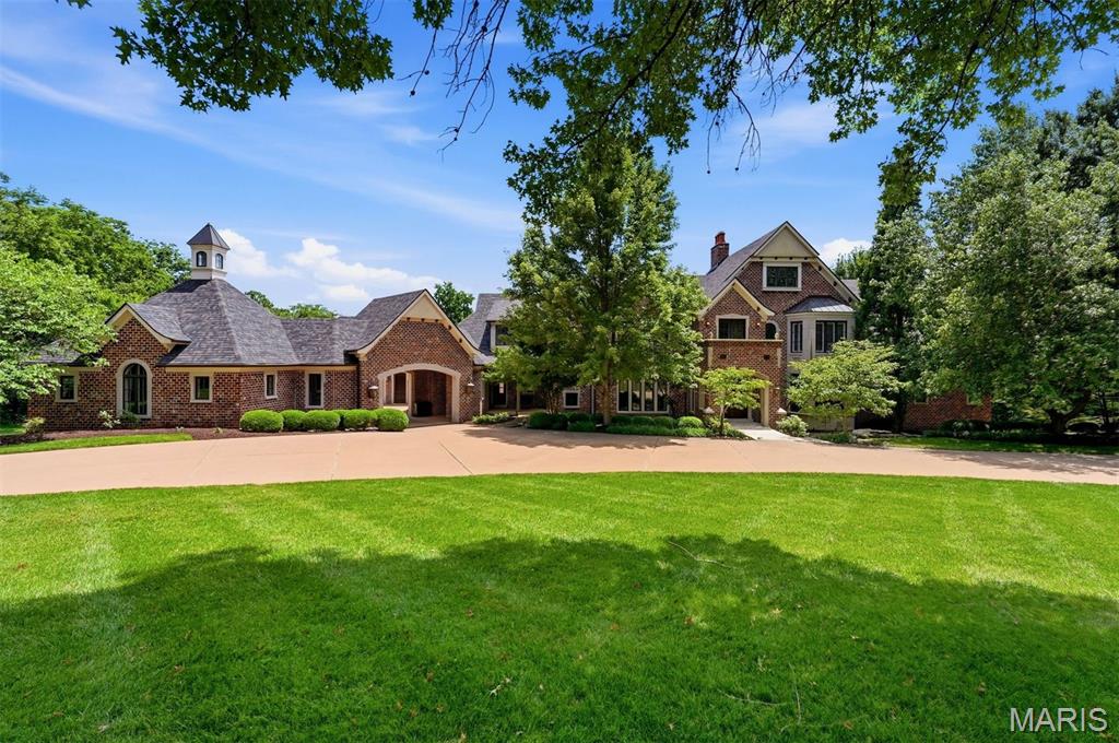 Ideally situated on a premier lane in one of Town & Country's most prestigious neighborhoods, this timeless estate, designed by Dick Busch, built by G. Terbock Luxury Homes, offers over 8,000 square feet of refined living space with 6 bedrooms, 7 full baths, 3 half baths, a 4-car garage, and porte-cochere, all nestled on spectacular park-like grounds. The grand foyer is highlighted by a sweeping staircase with custom wrought-iron balusters, and beautifully hand-carved newel posts, and a stunning two-story leaded-glass window that creates a breathtaking first impression. The handsome executive office is wrapped in custom hardwood paneling and distinguished by floor-to-ceiling built-ins, decorative fluted pilasters, extensive cabinetry, display shelving, and exquisite architectural detailing, while the formal dining room is enhanced by exquisite crown molding, and a decorative ceiling medallion. The impressive living room features a stunning mantel imported from France, a charming grand piano alcove, and walls of windows and French doors opening to the main-level terrace. Adjacent is a beautifully appointed bar with a striking copper ceiling, wine cooler, and temperature-controlled wine room. The chef's kitchen is thoughtfully designed with custom cabinetry, a 9-foot center island, Sub-Zero refrigerator, DCS ovens, a butler's pantry with dishwasher, and additional pantry with freezer. The sun-filled breakfast room flows seamlessly into the inviting hearth room, complete with a stone fireplace and handsome wood-paneled ceiling. A custom mudroom with built-in lockers, abundant storage, and direct exterior access leads to the 4-car garage, with a private guest suite above. The luxurious main-level primary suite is a true retreat, featuring a dramatic groin-vaulted ceiling with decorative crown molding, an elevated sitting room framed by arched windows, dual custom walk-in closets, and an exquisite marble bath with soaking tub, oversized shower, dual vanities, and a private pantry with refrigerator. The upper level offers a spacious junior suite, two additional bedrooms with en-suite baths, a comfortable sitting area with a beautifully detailed dark wood fireplace featuring carved columns, an intricately crafted mantel, and a distinctive green glazed tile, a reading nook with private terrace, laundry room, and is conveniently accessed by both front and rear staircases. Designed for recreation and entertaining, the walk-out lower level includes a spacious family room with cast stone fireplace, separate sitting area, golf simulator, fitness room, full bar, additional bedroom with en-suite bath, and an additional full bath conveniently located for pool guests. Outdoor living is equally exceptional, featuring a saltwater pool surrounded by lush, professionally landscaped grounds that create a private resort-like setting. Additional amenities include cherry hardwood and travertine flooring throughout, a whole-house programmable smart home system for security, lighting, and audio, zoned HVAC, irrigation system, and exceptional craftsmanship throughout. Perfectly located near premier hospitals, fine dining, shopping, parks, and major highways, this remarkable estate offers the rare opportunity to enjoy the tranquility of "country" living just minutes from everything the city has to offer.