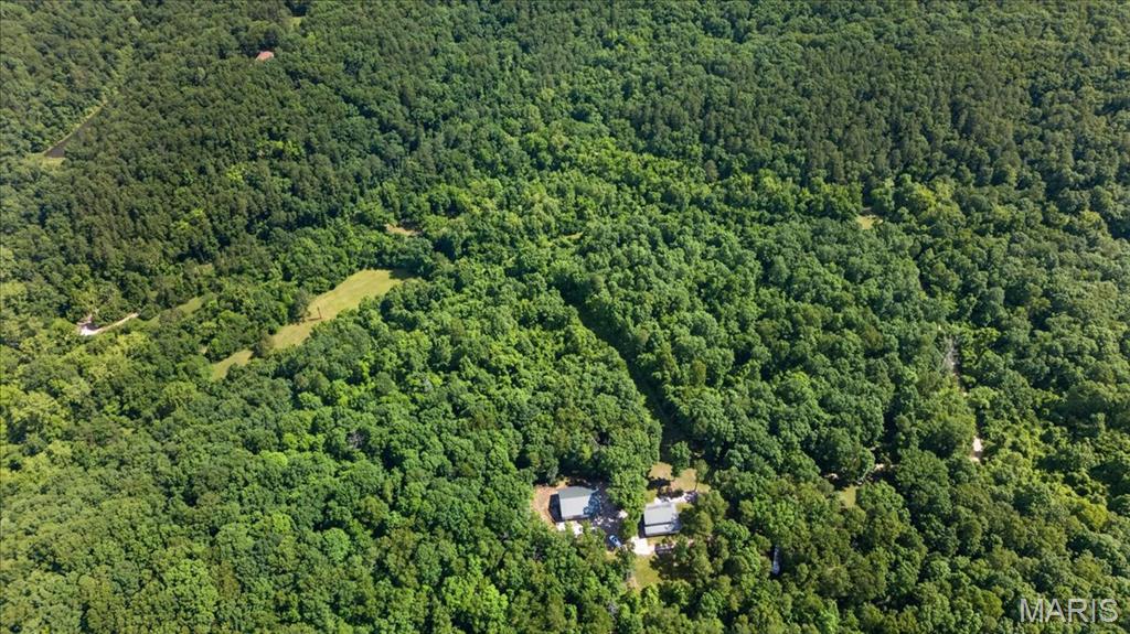 67 Acres of Privacy, Recreation and Scenic Hilltop Living. Welcome to your own private Missouri retreat. Nestled atop a scenic ridge and surrounded by 67 acres of predominantly wooded countryside, this remarkable property offers the perfect blend of comfortable living, outdoor recreation and unmatched privacy—all within an easy drive from St. Louis. A long private drive leads to the secluded homesite where a spacious 2200+ sq. ft. home overlooks the surrounding timber and rolling terrain. The inviting wraparound porch provides the perfect place to enjoy morning coffee, evening sunsets, and the peaceful sights and sounds of nature. Inside, you'll find an open floor plan with spacious living, dining, and kitchen areas designed for everyday living and entertaining. The main level includes the primary bedroom, full bath, laundry, and utility room, while the upper level offers two additional bedrooms, a second full bath and a versatile bonus room ideal for guests, a home office or hobby space. Outdoor enthusiasts will appreciate the established trail system, multiple deer stands, rolling wooded terrain and two creeks that wind throughout the property, creating excellent wildlife habitat and endless recreational opportunities. Whether your passion is hunting, ATV riding, hiking, target shooting, wildlife watching or simply exploring your own land, this property is designed to be enjoyed year-round. A standout feature is the impressive 40' x 40' insulated outbuilding complete with electric service, concrete floors and three 10' x 12' overhead doors—offering exceptional space for tractors, equipment, recreational vehicles, workshop projects and storage. The recently acquired adjoining 10-acre parcel expands the property to approximately 67 acres, enhancing privacy and creating even more opportunities for recreation, future improvements or simply enjoying the freedom of owning your own piece of Missouri countryside. Whether you're seeking a full-time residence, weekend escape, hunting retreat or legacy property to enjoy for generations, this rare offering combines scenic beauty, usable improvements and recreational opportunities in a setting that is becoming increasingly difficult to find.