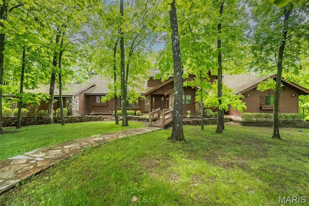 Tucked away on 5 breathtaking acres in the heart of Wildwood, this extraordinary lodge-inspired estate offers a lifestyle few properties can match. Surrounded by towering hardwoods and complete privacy, the setting feels more like a mountain retreat than a St. Louis address.

Inside, over 5,000 square feet of living space unfolds beneath soaring wood-beamed ceilings, dramatic timber accents, and walls of windows that bring the beauty of the outdoors inside. The stunning great room serves as the heart of the home, anchored by a floor-to-ceiling stone fireplace and framed by an impressive open staircase and loft overlook that create a true "wow" moment from the moment you enter.

Designed for both everyday living and unforgettable entertaining, the spacious kitchen offers abundant cabinetry, a center island, and seamless flow into gathering spaces filled with warmth and character. Multiple fireplaces, expansive living areas, and wooded views from nearly every room create an atmosphere that is both grand and inviting.

The main-level primary suite is a private sanctuary featuring a spa-inspired bath, generous walk-in closet, and peaceful views of the surrounding landscape. With 5 bedrooms, 4.5 baths, and a finished walk-out lower level complete with additional recreation space, there is room for family, guests, hobbies, and multigenerational living.

Step outside to discover expansive decks, winding pathways, mature trees, and a setting that changes beautifully with every season. Whether enjoying morning coffee among the treetops, hosting gatherings under the stars, or simply appreciating the quiet beauty of nature, this property delivers a rare sense of escape.

A truly one-of-a-kind offering where rustic elegance, timeless craftsmanship, and unmatched privacy come together on one spectacular Wildwood estate!