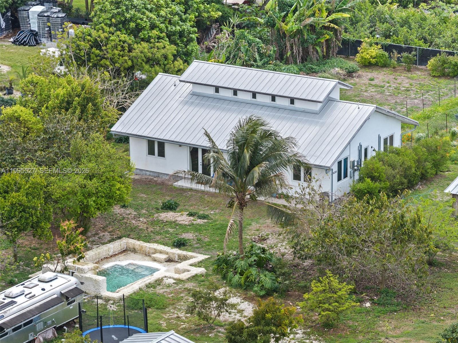 Tucked away on 1.54 lush acres in the Redlands, this thoughtfully designed eco-friendly, owner-built estate blends sustainability with serene living. Completed in 2022, the 3BD/2BA residence offers 1,500 SF plus a charming 200 SF loft—ideal for office, studio, or retreat—accessed by a beautiful wood staircase. Enjoy a light-filled interior, solar panels, and two potable wells for home and agriculture. Outdoors, discover an agricultural pond with waterfall, greenhouse, three outbuildings, and organic garden. A tropical paradise with over 60 tree orchard including mango, avocado, lychee, mamey, jackfruit, and more—Enjoy your private farm-to-table sanctuary.