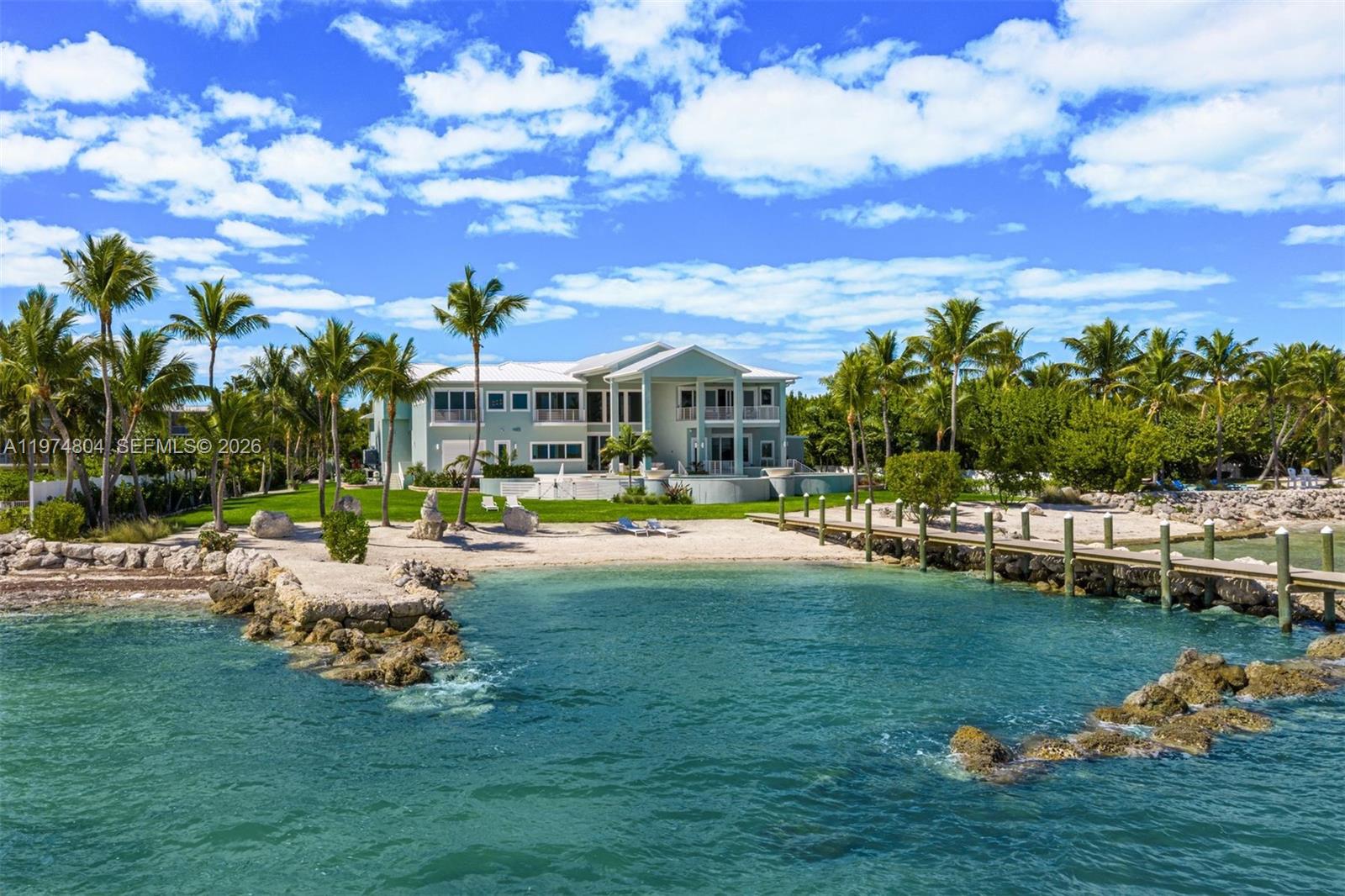 Newly completed in 2025, this exceptional oceanfront estate is located in the heart of The Florida Keys on the premier ocean side of Islamorada. A gated entry welcomes you through lush tropical landscaping and a diverse fruit-tree grove, setting a private and refined arrival. Set on over 2 usable acres with 210 feet of private sandy beachfront and a protected cove, the residence spans 7,590 square feet of interior living space & 1,736 square feet of exterior living, with an expansive 230-foot dock. Designed for seamless indoor-outdoor living, the home features a dramatic great room with 23-foot ceilings, panoramic Atlantic exposure, and expansive covered terraces with summer kitchen and outdoor dining areas. A 65-foot heated lagoon-style pool with swim-up bar and fire-pit lounge creates a resort-caliber setting. The chef’s kitchen is appointed with Sub-Zero, Wolf, and Thermador appliances. Additional highlights include dual primary suites, private orchid garden, lounge & recreation room, elevator, Sonos surround sound, impact windows and doors, metal roof, double-height garage, water-sports storage room and a full home generator. The essence of beachfront living in Islamorada, combining impressive scale and ultimate privacy. ***A contiguous 0.7-acre lot with development rights for an ancillary building with upstairs storage is available separately.