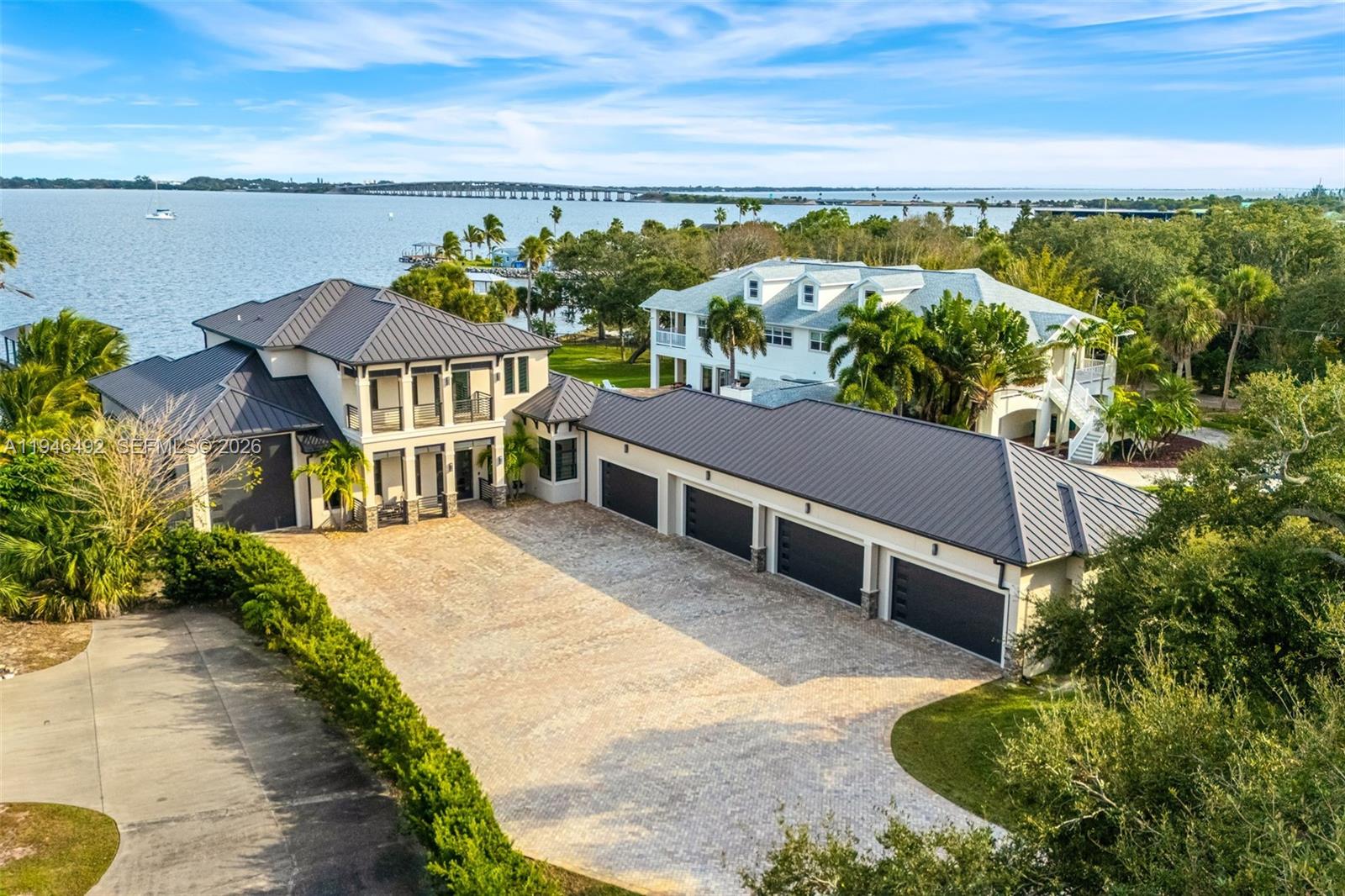 The ultimate private classic car showroom and motorcoach retreat. This stunning custom riverfront home features a massive 8-car garage which includes a 10,000 lb tandem lift for your curated vehicle collection, and an additional high-clearance, 55 ft RV/boat garage offering full hookups. This mariner's paradise also offers 110 ft open water frontage with a granite rock shoreline and direct views of the intracoastal river. The custom dock includes 2 lifts to accommodate up to a 30 ft boat with shore power, and a personal watercraft lift. This enhanced solid poured concrete exterior, freshly painted and sealed, 5 bed 4.5 bath home offers a vibrant coastal lifestyle with an infinity edge saltwater pool and built-in spa, large covered porch and summer kitchen with custom Kalamazoo cabinetry and marine grade stainless steel grille. Seamlessly blending indoor and outdoor living with impact sliding glass pocket doors in the great room and the primary suite for expansive river views, artisanal finishes like custom imported marble floors, and a spa-like ambiance of the primary suite which includes a custom walk-in steam shower and a freestanding soaker tub, and a massive walk-in closet leading to the laundry room. The chef’s kitchen features a 15 ft quartz island with waterfall edges, massive side by side fridge and freezer, but the hidden butler’s pantry steals the show. Bespoke design meets timeless character, highlighted by vintage cathedral doors and even a salvaged ship’s door.
