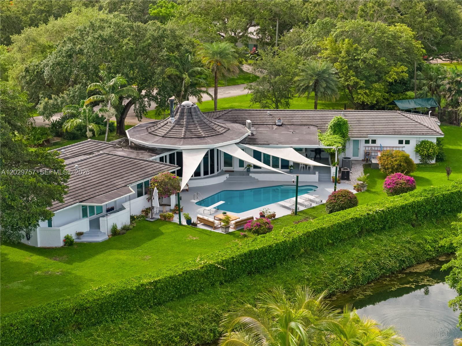 Welcome to the newly refreshed and re-priced Casa Rotonda! This striking Barry Sugarman-designed canal front estate sits on a builder’s acre in the heart of Pinecrest. It is a rare blend of architectural pedigree, thoughtful updates, and timeless design. Spanning over 5,000 square feet, the residence offers five bedrooms and five baths, including private staff quarters. The interiors have been beautifully refreshed, featuring rich cherry hardwood floors, marble finishes, and custom Italian doors. The chef’s kitchen is both functional and stunning, equipped with double Wolf gas ovens, an oversized Sub-Zero refrigerator, and a generous workspace designed for both everyday living and entertaining. Walls of impact glass open to a resort-style outdoor setting with a sparkling pool, expansive grounds, and tranquil canal views, enhancing the home’s sense of privacy and scale. A three-car garage, a newer roof, and proximity to top schools, trails, and the bay further elevate the offering. This is a home for those who appreciate architecture, space, and one of Pinecrest’s most desirable waterfront settings. Luxury, design, and location in perfect harmony, and an exceptional opportunity to own a truly distinctive property.