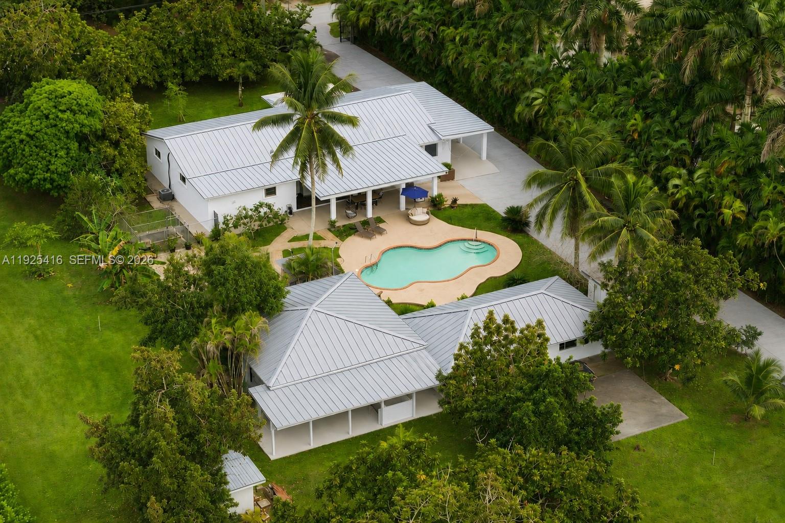 Tucked behind lush landscaping in the heart of the Redlands, this 2.42-acre tropical retreat offers a rare blend of serenity, recreation, and resort-style living. The 3-bed, 2-bath main residence features spacious interiors with open living areas, garden views, and a seamless indoor-outdoor flow. Across from the main house sits a detached game room/studio suite with full bath, plus a separate entertainment pavilion which boasts a bar and grill, as a covered lounge. Outside, enjoy a sparkling kidney-shaped pool surrounded by fruit trees, flowering gardens, and shaded patios. Located at the back of the property, sits a 2-car garage with a connected 1-bed/1-bath apartment. The grounds are a horticultural haven with more than a dozen varieties of tropical fruit trees, mature palms, and lush plantings that create a true sense of escape. Designed for both relaxation and activity, the property includes stables to board 5-horses, and a rare private indoor sports shooting range. Additional features in the main house include a formal dining area, dual primary suites, whirlpool tub, accordion shutters, and a full-house generator for peace of mind. As a family compound, private getaway, or equestrian paradise, this exceptional estate delivers a unique lifestyle immersed in the natural beauty and privacy of South Florida’s iconic Redland agricultural community.