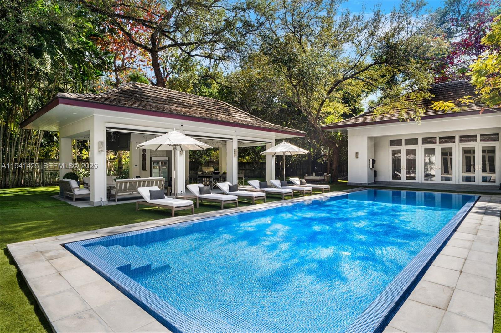 Set behind lush landscaping on approximately 1.1 acres in South Coconut Grove, this expansive one-story residence delivers 11,766 total SF with 6 bedrooms, 7 full bathrooms, and a powder room. Designed for comfort and effortless entertaining, the home showcases 12-foot ceilings, wide-plank wood floors, impact French doors, and refined architectural detailing throughout. Multiple living areas include formal and casual spaces, a wet bar, staff quarters, and a showpiece kitchen outfitted with custom cabinetry, quartz surfaces, a walk-in pantry, and a full set of premium Wolf, Sub-Zero, and Miele appliances. Two generous primary suites feature private sitting area, office, spa-style marble baths, and custom walk-in closets. The outdoor setting feels like a private resort, offering covered terraces, a heated pool, a separate oversized spa, half basketball court, volleyball court, outdoor entertaining areas, and a detached guest house currently configured as a gym. Additional features include a 4-car garage, whole-home generator, advanced smart home and security systems, and expansive grounds ideal for refined Grove living.