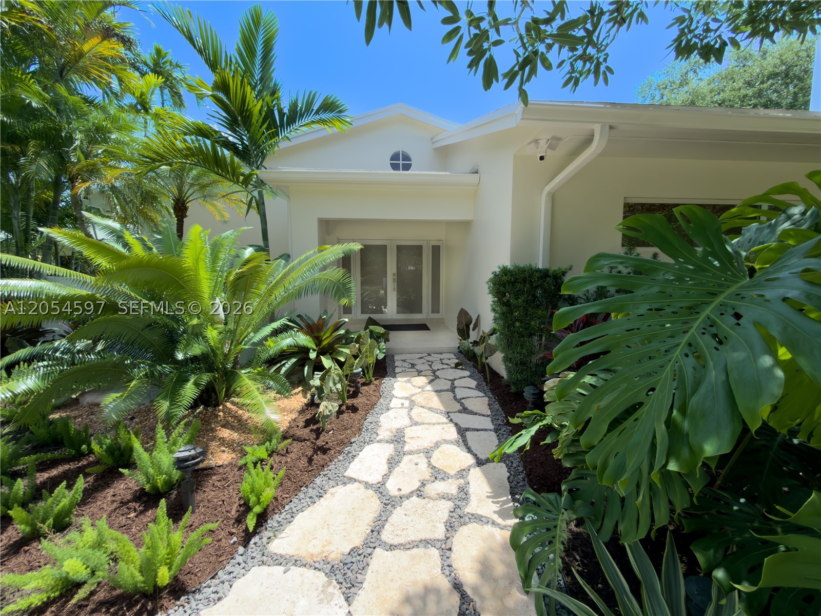 Beautifully reimagined with a refined contemporary aesthetic, this light-filled residence showcases soaring wood-clad ceilings, abundant natural light, and an open-concept layout designed for effortless living and entertaining. The chef's kitchen features custom millwork, generous prep space, and a walk-in pantry. The private primary suite offers a spa-inspired bathroom with designer finishes, creating a serene retreat. Surrounded by lush tropical landscaping, this thoughtfully designed, Apple-integrated smart home blends timeless design with the relaxed South Florida lifestyle.