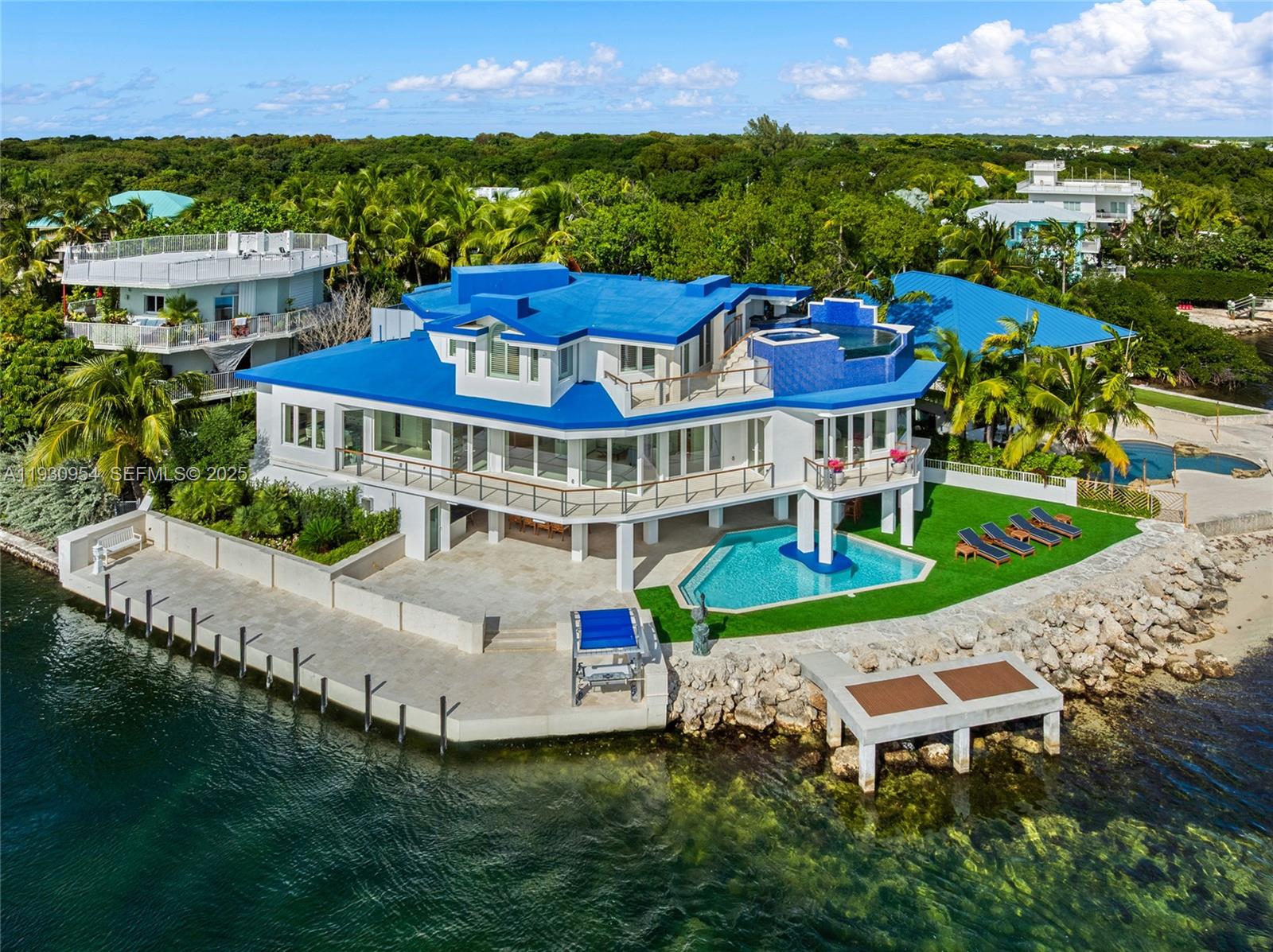 This 2-story estate sits on a 7,300 SF point lot at the tip of Adam’s Cut w/167 FT WF & views to Largo Sound w/ocean access. Spanning 3,723 SF the 4BR/5+2BA home features La Finestra impact windows, elevator & Shell Reef limestone floors. 1st floor offers living room w/floor-to-ceiling windows, drop-down TV, terrace access, open dining area, & chef’s kitchen w/backlit polished Plume Quartz island & top-tier Jenn Air appliances. 3 BRs include a junior suite w/private balcony plus 2 ensuite guest rooms. 2nd-floor principal suite has an additional room, lux spa-style bath, & private terrace w/rooftop infinity pool-jacuzzi, & bar. Ground-level highlights: Large covered terrace, summer kitchen, pool, bar, cabana bath, & wine cellar. 77 FT dock w/permitting in progress for a 30,000 lb boat lift.