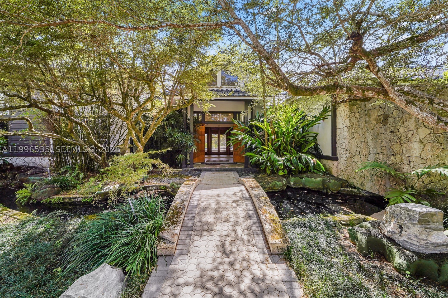 Tucked away in the heart of the Redlands, this private estate spans just over 4 acres of agriculturally zoned land surrounded by mature landscaping and a tranquil Japanese-inspired garden complete with a bridge, cascading water feature, and koi stream. The residence offers 4 bedrooms, 5 full bathrooms, and a newly renovated half bath, with expansive living spaces featuring soaring ceilings, a coral rock fireplace, an updated kitchen, formal dining room, spacious family room, and views overlooking the courtyard and pool. Each bedroom offers direct exterior access, while covered terraces, a large screened patio, game room with bar, built in BBQ, and a newly constructed pickleball court create an exceptional indoor outdoor lifestyle. The grounds are a true tropical oasis, featuring approximately 110 avocado trees, 2 mango trees, 3 lychee trees, 6 star fruit trees, 1 loquat tree, and wild guava growing throughout the property, providing both agricultural value and an incredible variety of homegrown fruit. With its distinctive architecture, private setting, income producing grove, and endless possibilities, this exceptional estate presents a rare opportunity for end users, investors, or anyone seeking a one of a kind South Florida retreat.