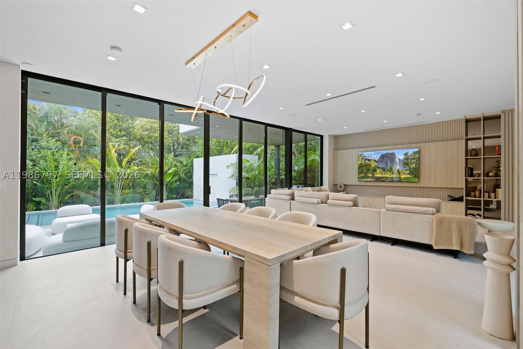 Welcome to the Modani Residence, a showcase of modern design and turnkey luxury in the heart of Miami Beach. This stunning five-bedroom home is offered FULLY FURNISHED with Modani furniture and thoughtfully curated designer finishes throughout, with a serene atmosphere created by neutral palettes and greenery. A grand atrium-style entry with a striking staircase sets the tone upon arrival. The main level features open-concept living, connecting the formal living room with double-height ceilings, family room, dining area, and chef’s kitchen. The kitchen is equipped with premium Miele appliances, including a gas range stovetop, dual dishwashers, refrigerators, and sinks. A first-floor bedroom adds flexibility for guests or office use, while laundry is located in the garage. The home also offers a two-car garage and a large driveway with a coral stone design. Upstairs, four generously sized bedrooms each feature ensuite bathrooms and custom built-ins. Two bedrooms open to a front-facing balcony overlooking the front yard, while another sits privately to the side. The expansive primary suite overlooks the backyard and pool, complete with its own balcony, a large custom walk-in closet, dual vanities, and a separate tub and shower. The backyard is designed for entertaining, with a large pool, cabana bathroom, and patio area. A truly one-of-a-kind residence, offered fully furnished for a turnkey lifestyle with a sense of calm, design, and distinction.