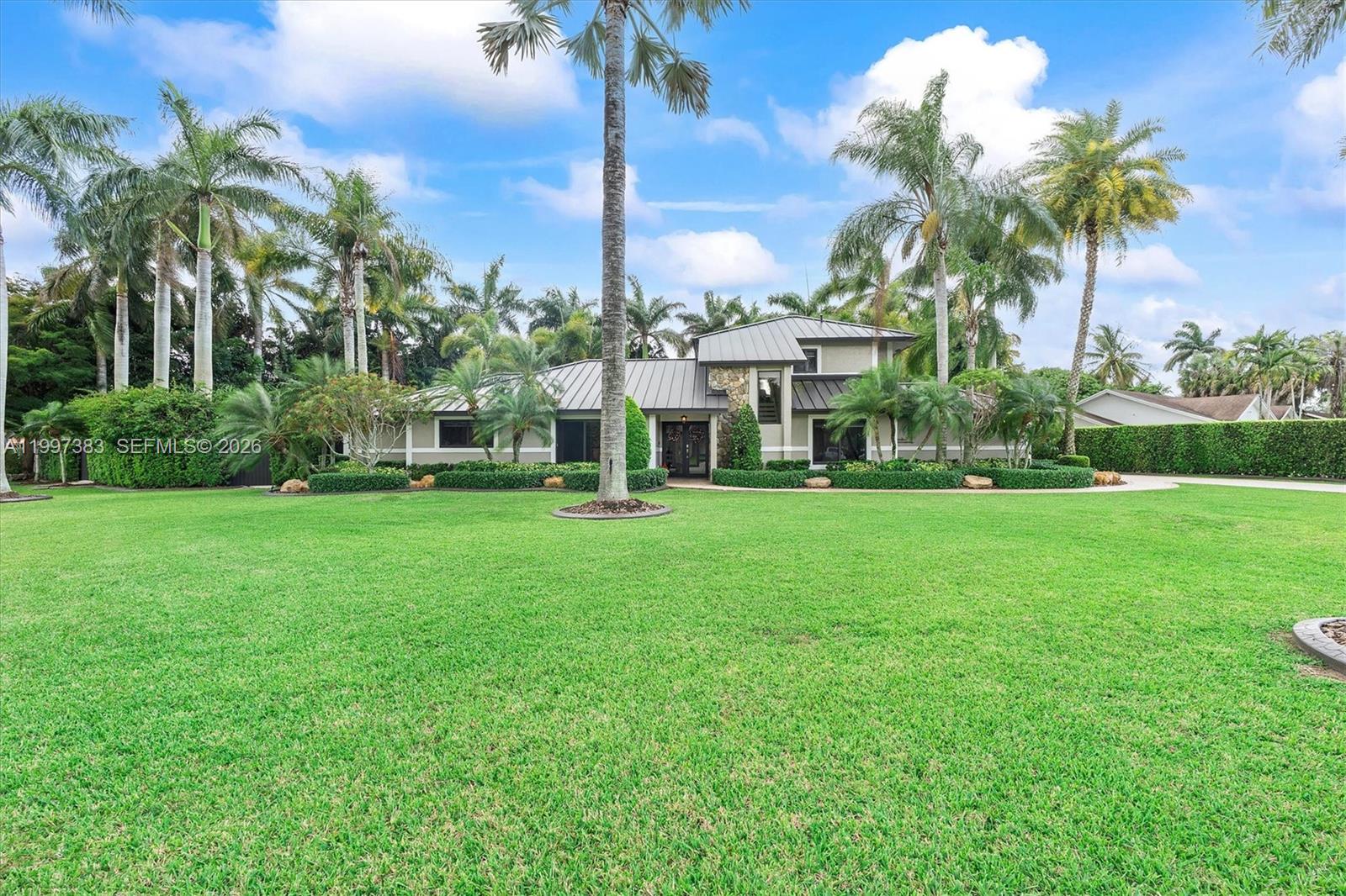 Luxury Compound with Resort Backyard + Climate-Controlled Workshop. 

Experience a rare opportunity to own a private half-acre corner estate in Kings Grove—where luxury living meets unmatched functionality. This fully built-out lifestyle property is designed for entertaining and relaxing at a higher level. The residence offers 3,188 sqft of completely remodeled living space, featuring a new standing seam metal roof (2023), impact windows/doors, and high-end finishes. The centerpiece kitchen impresses with a 10-foot island, waterfall Arctic White granite, and premium KitchenAid appliances, flowing into open living areas.

The resort-style backyard, completed in 2025, features a heated pool and spa with beach entry, a custom rock waterfall, and a 25x25 rethatched tiki hut. Enjoy the outdoor kitchen with FireMagic appliances, a Sonos sound system, and a private putting green. Surrounded by lush tropical landscaping and over 20 Royal Palms, the property delivers total privacy and a true South Florida feel. For collectors or hobbyists, the estate includes a 1,250 sqft climate-controlled workshop with a professional car lift and high-gloss floors—a rare addition that sets this home apart. Additional features include smart home integration, updated designer bathrooms with Carrara marble, and multiple A/C systems. This property combines land, luxury, and utility in a complete package located near premier shopping and amenities.