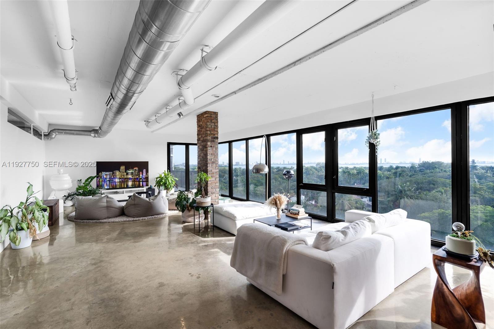 Discover this one-of-a-kind loft-style 4BD/3.5BA residence—currently configured as a 3-bedroom plus storage—offering dramatic open-concept living, sweeping floor-to-ceiling glass, and panoramic views of Biscayne Bay, the Miami skyline, and lush tree canopies. Designed with an industrial-modern aesthetic, the home showcases exposed ducts, polished concrete floors, brick accents, and custom wood millwork throughout. The expansive great room seamlessly integrates living, dining, and an open chef’s kitchen, creating an ideal setting for entertaining. The primary suite delivers a true retreat with incredible natural light, oversized balcony access, and a sculptural soaking tub set against skyline vistas. Multiple lounging areas, flexible spaces perfect for office or creative use, and generous storage enhance daily living. The boutique building offers two elevators, just 3–4 residences per floor, a rooftop dry sauna, and pool, and is just a 3-minute walk from beautiful Morningside Park—offering an exceptional blend of volume, character, lifestyle, and location at the edge of Morningside and the MiMo District.
