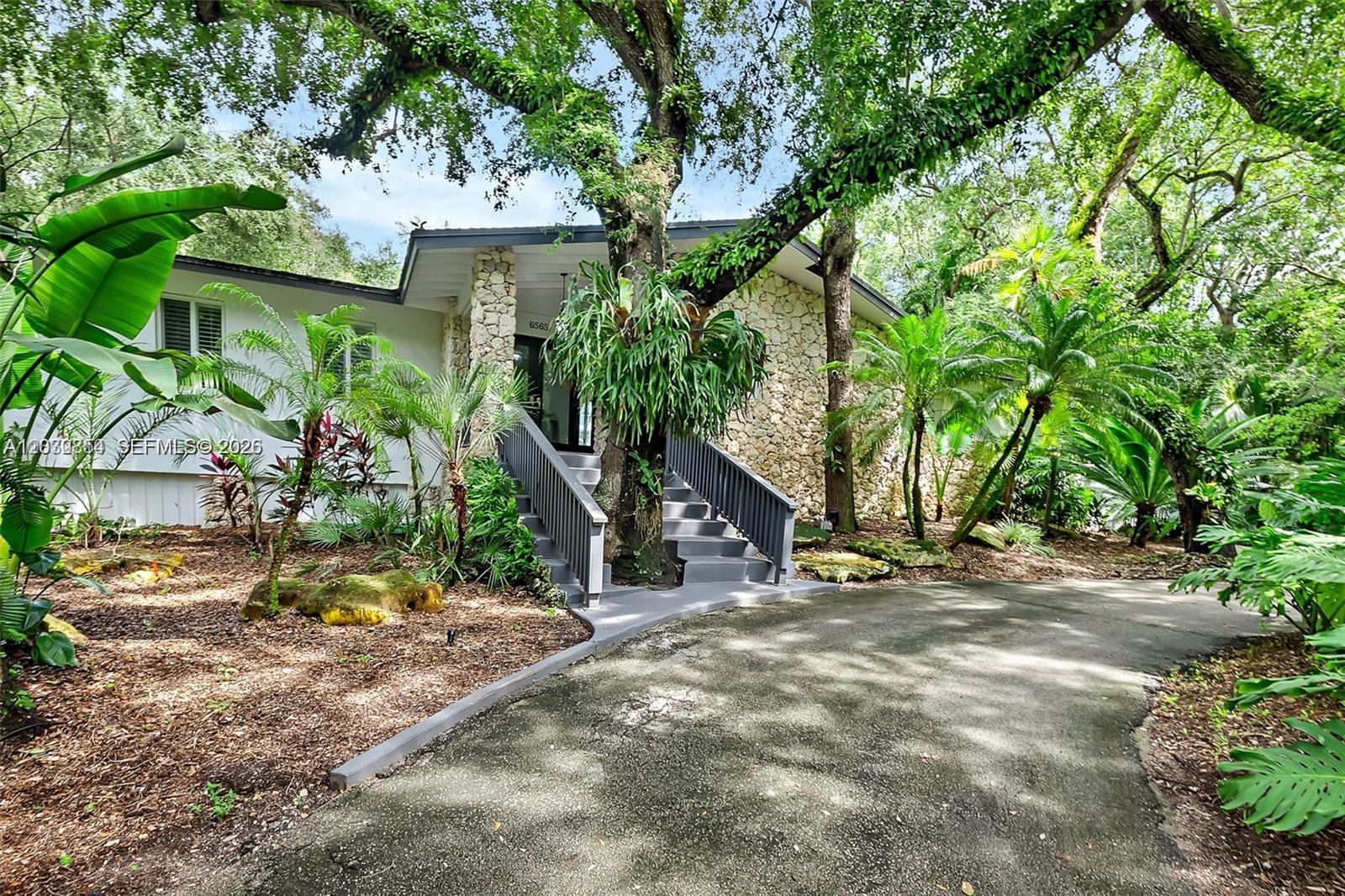 Nestled on a lush half-acre corner lot in the highly desirable Devonwood neighborhood, often referred to as the "Coconut Grove of Pinecrest," this unique residence offers the perfect blend of privacy, nature, and modern living. Elevated to capture tranquil treetop views, the main living areas are surrounded by tropical landscaping, creating a true retreat-like setting.

The chef’s kitchen features custom cabinetry, premium Bosch appliances, a massive island, and stunning natural stone waterfall countertops. Floor-to-ceiling recessed aluminum doors seamlessly connect indoor and outdoor spaces, filling the home with natural light. Entertain with ease in the stylish wet bar, brand-new outdoor kitchen, and covered terrace ideal for al fresco dining.

The spacious primary suite offers dual custom closets, built-in cabinetry, and a spa-inspired bathroom. The versatile lower level includes a sauna and atrium area perfect for a private wellness retreat, plus a large flexible-use room ideal for a home theater, fitness studio, recreation room, or additional living space.

A rare opportunity to enjoy luxury living surrounded by nature in one of Pinecrest’s most sought-after neighborhoods.