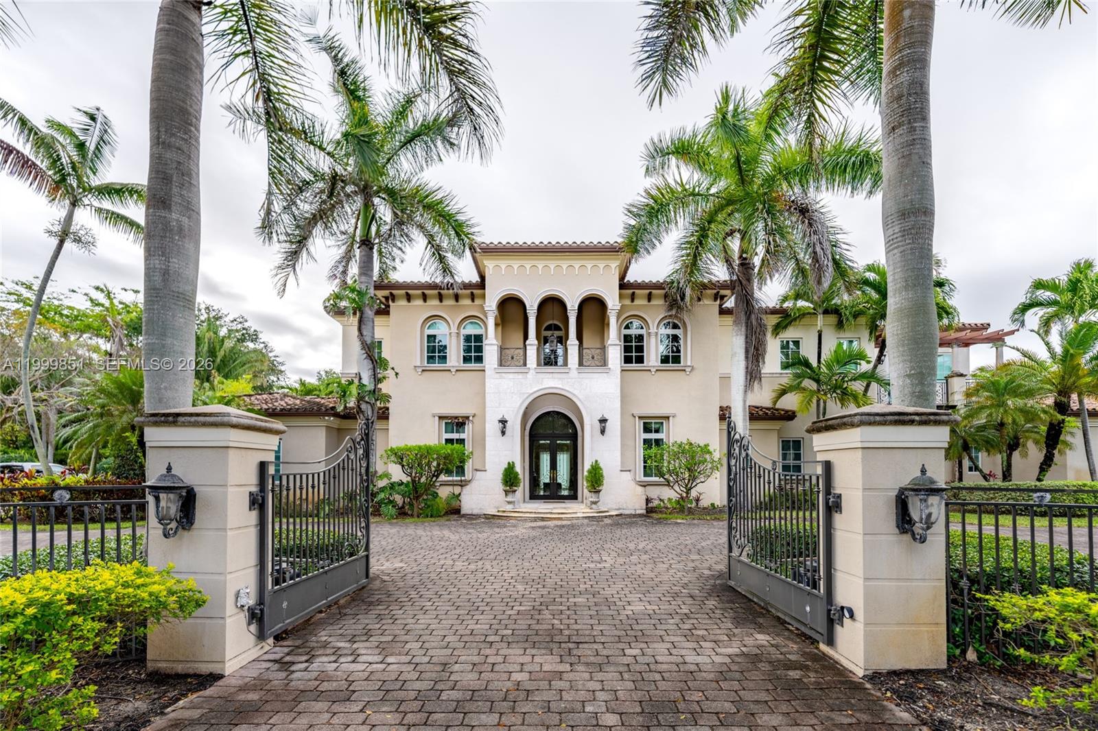A statement of timeless elegance and architectural grandeur, this Mediterranean-inspired estate welcomes you through a gated entrance framed by majestic royal palms and a sweeping circular driveway. The striking façade showcases symmetrical design, arched windows, and a second-story balcony that sets an impressive tone of refinement.
Step inside to a breathtaking double-height foyer featuring a dramatic curved staircase with wrought-iron detailing, gleaming marble floors, and a grand arched entry door that fills the space with natural light. Every element reflects meticulous craftsmanship and a sense of arrival.
The main living areas are designed for both comfort and sophisticated entertaining, highlighted by soaring ceilings, expansive open spaces, and elegant archways that seamlessly connect each room. The formal living room exudes warmth and luxury, complemented by a second-floor balcony overlook that enhances the home’s open, airy ambiance.
Architectural details such as custom iron railings, columns, and curated finishes elevate the interiors, while large windows and glass doors invite in natural light and offer tranquil views of the lush surroundings.
This residence embodies the essence of South Florida luxury living—grand yet inviting, refined yet comfortable—offering a perfect setting for upscale entertaining and everyday elegance.