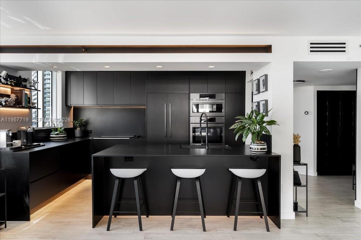 This fully reimagined bayfront corner 2-bedroom, 2-bath residence on Miami Beach’s serene West Avenue reflects a level of craftsmanship and intention typically reserved for a designer’s own home. The bespoke renovation features black leathered granite countertops and backsplash, custom cabinetry, Bosch appliances, and sleek integrated ambient lighting throughout. High-end matte black bath fixtures and thoughtfully built-out his-and-hers closets complete a tranquil, refined retreat, where every detail has been curated with both elegance and everyday comfort in mind. The full-service building offers two pools, a state-of-the-art gym, concierge, and valet services. From the wraparound balcony, enjoy Canopy Park and city views with partial bay vistas, along with a future pedestrian bridge connecting directly to South of Fifth. The residence may be offered turnkey as an option, presenting a seamless opportunity for elevated Miami Beach living.