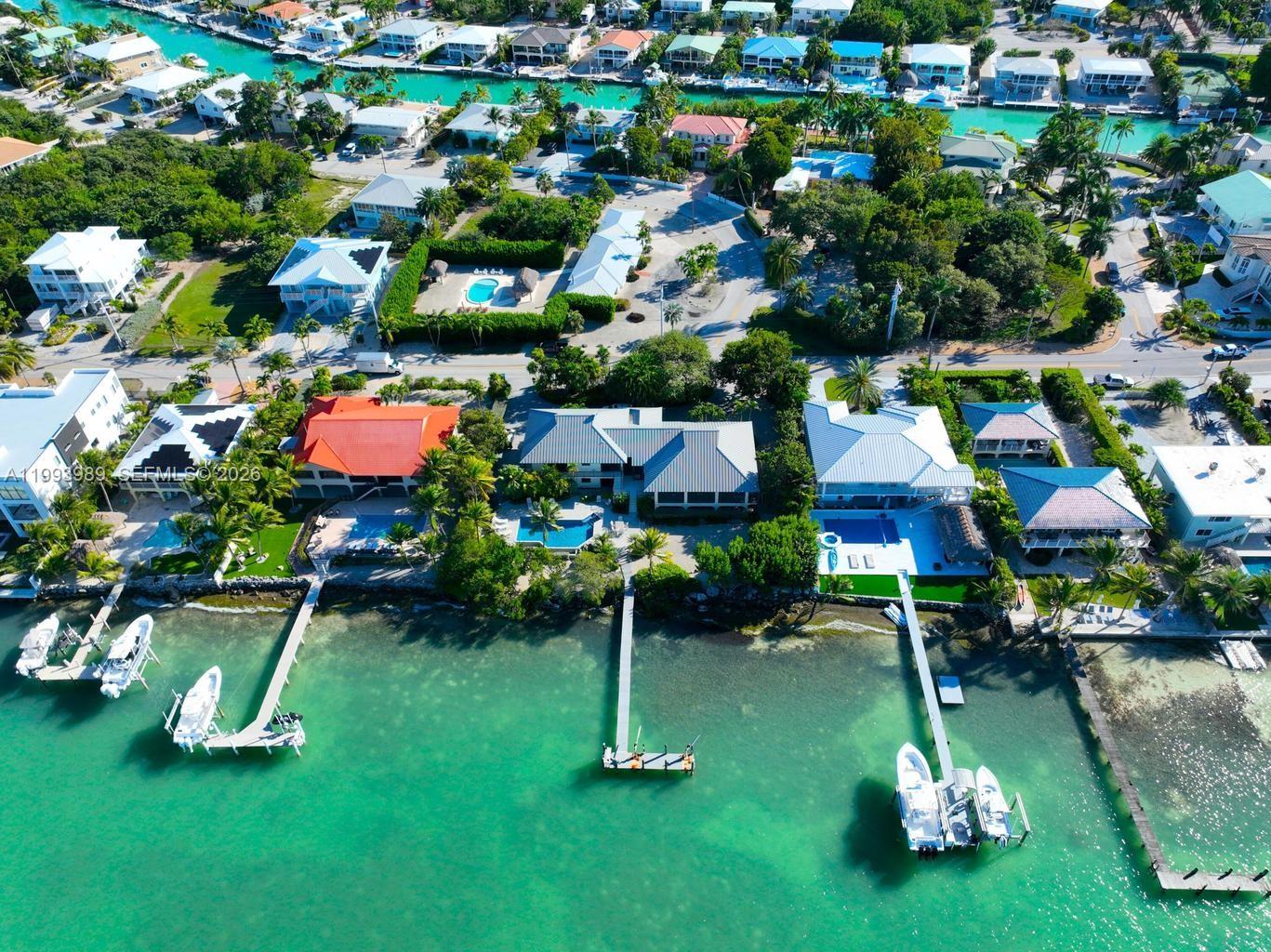 First time ever offered, this extraordinary open-water estate commands a premier position on Duck Key overlooking the crystal-clear waters of Tom's Harbor and iconic bridge. Spanning two expansive lots with an impressive 152 feet of water frontage, this iconic residence—designed by renowned architect Dale Baldwin—delivers rare scale, privacy, and timeless Florida Keys elegance. A dramatic double-door entrance opens to a light-filled open floor plan defined by white-washed vaulted and tray ceilings, walls of windows, and sweeping harbor views. The chef's kitchen features black granite countertops, a statement island, butler's pantry, and premium appliances including Thermador double ovens, Jenn-Air cooktop with grill, Whirlpool French-door refrigerator, and GE trash compactor. A formal dining space for twelve, pass-through bar and billiards area, and spacious living zones create an exceptional environment for elevated entertaining overlooking the water. The oversized primary suite offers a private waterfront retreat with spa-inspired bath, expansive walk-in closet, and balcony overlooking open water. All bedrooms enjoy private balconies. Additional highlights include abundant storage, interior stairways, laundry room, white ceramic tile floors, and plush carpeted bedrooms. Outdoors, a screened balcony, resort-style pool with paver deck, and mature tropical landscaping frame the ultimate island lifestyle. The expansive T-dock provides outstanding versatility for a boat lift, jet ski lift, and kayak launch. Built with solid concrete construction, standing-seam metal roof, accordion shutters, subfloor access, two-car garage, and a grand half-circular driveway. A landmark offering where architectural distinction meets open-water serenity on prestigious Duck Key.