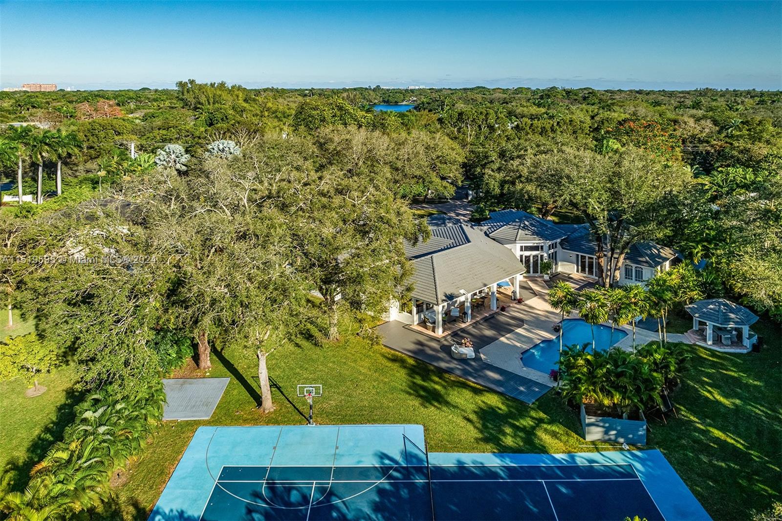 Recently renovated 7,167 SF residence in North Pinecrest, with 6-BD and 6.5-BA on an impressive 1.36-acre lot, surrounded by mature oak trees providing optimal privacy and seclusion. The home offers a spacious layout with volume ceilings, two family rooms, and marble and wood flooring throughout. An expansive updated gourmet kitchen boasts ample counter space, quartz countertops, a large center island, walk-in pantry, and all-new appliances. The backyard retreat features a covered terrace, tennis court, pool cabana with a built-in grill and gas range, and a sparkling pool with a waterfall jacuzzi. Additional features include renovated bathrooms, new interior doors, 3 AC units, flat tile roof, 3-car garage, and a whole-house generator.