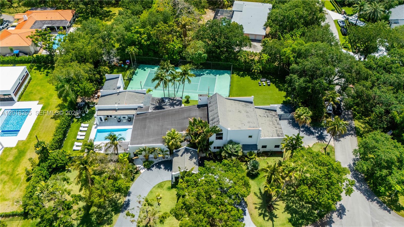 A fully reimagined corner estate in the sought-after Baptist Hospital area — set on over an acre of private, manicured grounds. The main residence delivers on every level: double-height ceilings, a floating black marble and glass staircase, bold Italian kitchen with Fulgor Milano appliances, starlit home theater and sauna. The primary suite is a true retreat: soaring ceilings, a private balcony, dual walk-in closets, and a spa-caliber marble bath with glass-enclosed shower and backlit vanity. Two additional en-suite bedrooms complete the upstairs. Outside, a newly built pool is surrounded by a resort-style terrace, covered outdoor kitchen, full-size tennis court, and lush turf lawn. Two independent guest structures — a 2/2 back house and a 1/1 cottage with kitchen — plus a 4-car garage make this a true compound.