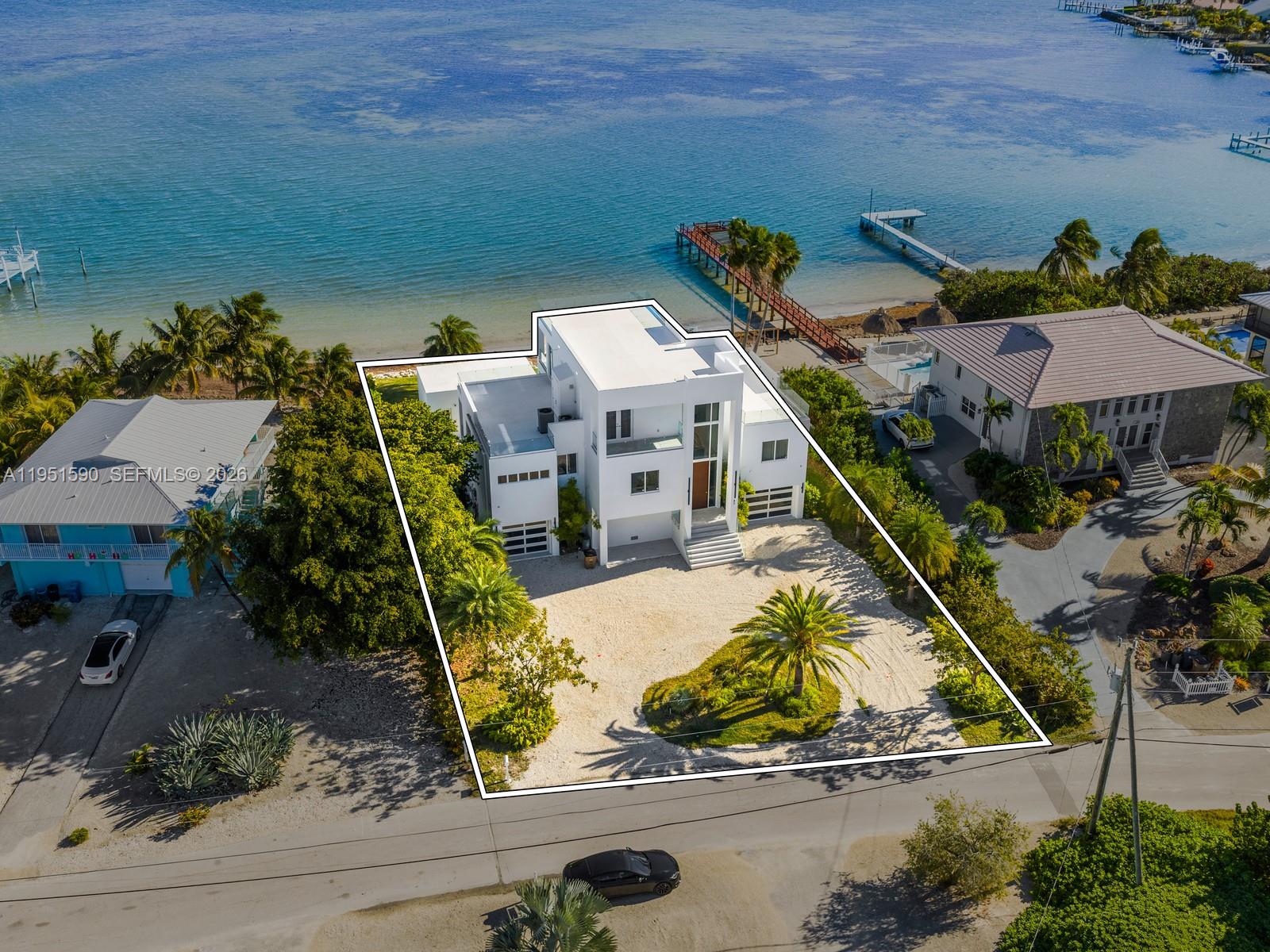 Where every day feels like a five-star vacation. At first glance, the home captivates with its contemporary exterior, natural landscaping, circular driveway, and a jaw-dropping front entrance that feels more like a private resort than a residence. Inside, nearly every space is wrapped in ocean views and natural light. The sun-filled living room features dramatic accordion glass doors that open to a balcony overlooking the backyard, pool, and endless blue horizon. It’s a space where mornings feel peaceful and evenings melt into golden sunsets. The kitchen is both beautiful and functional, designed for gathering. Crisp white cabinetry, stunning stone counters, high-end stainless appliances, and a large waterfall island make it perfect for everything from casual breakfasts to entertaining.

Step outside and prepare to fall in love. The covered patio is ideal for dining and relaxing with views of the pool, a grilling area, and the sparkling ocean beyond. A rock retaining wall leads to a crystal-clear beach, your own private escape just steps away. The primary suite is a true sanctuary with water views, a private balcony, and a spa-like ensuite with a tiled shower and a massive walk-in closet. Additional bedrooms offer beautiful scenery, while the elevator provides easy access to the unforgettable rooftop deck with panoramic ocean views and magical sunsets. Get ready to embrace the Florida Keys lifestyle with ocean breezes, sunsets, and living every day in paradise.