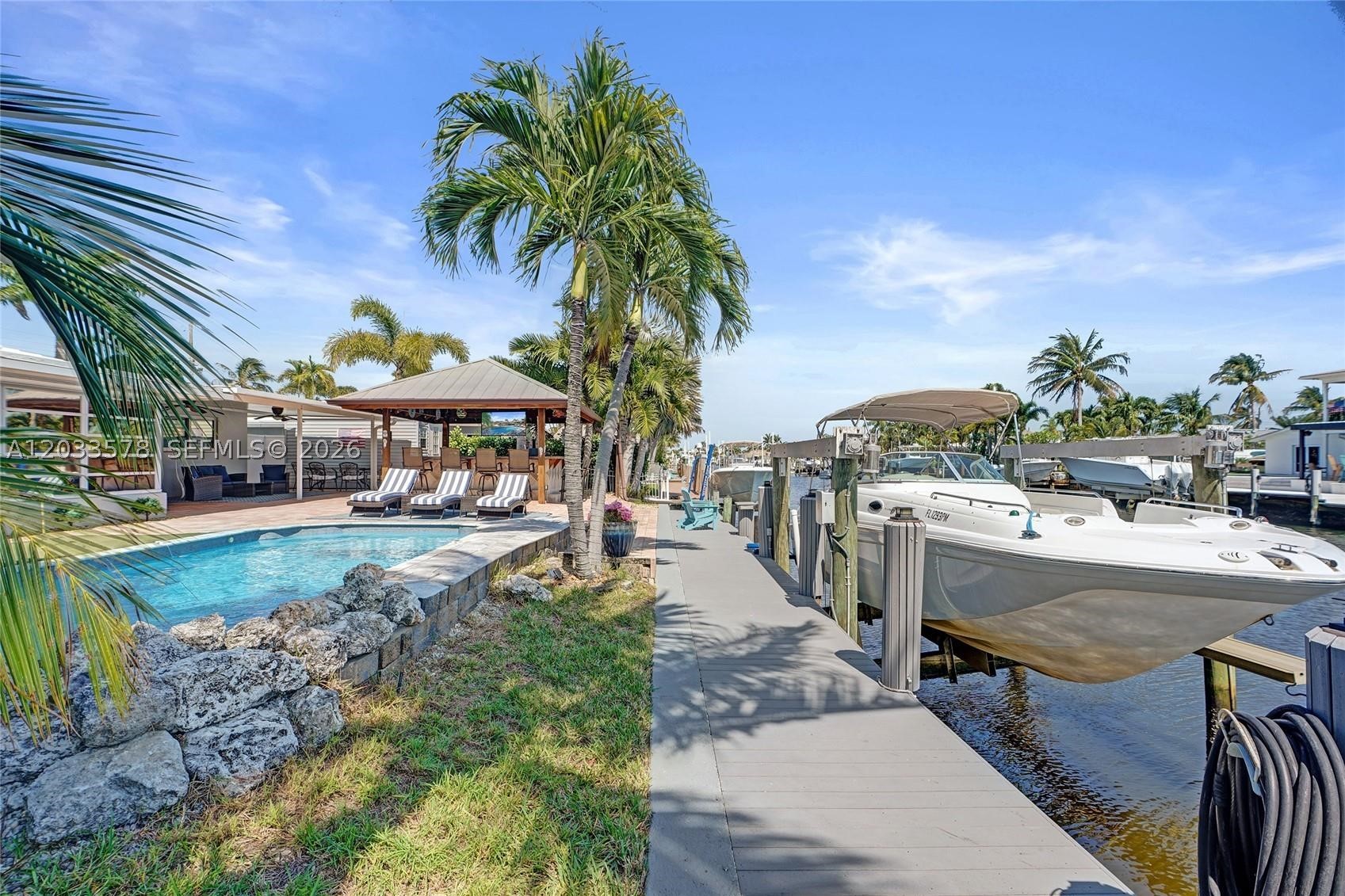 The Ultimate Boater's Oasis in Garden Isles–Waterfront Luxury Re-imagined. Rare double-wide canal making navigation a breeze. Enjoy direct ocean access just minutes from the open ocean and unique gated parking area for RV or other toys. RARE 75 ft water frontage and upgraded boat lift. Only 2 fixed bridges w/ high clearance on a quiet, no-thru traffic street perfect for children, grandchildren & dog walking, this remodeled 3-bed 2-bath Smart Home offers the perfect blend of tropical relaxation and high-tech convenience (Smart features include Voice-operated or by cell phone> door locks, ceiling fans, lighting, appliances & thermostat. Entertainer's dream w/ outdoor tiki bar w/ metal roof and professional-grade outdoor kitchen w/ running water. Whether you’re hosting a summer BBQ or practicing your short game on the custom putting green surrounding the pool, the outdoor lifestyle here is unmatched. After sunset, unwind in the 5-person hot tub or find peace in the lush reading garden filled with blooming roses. Features a rare 32x12 ft gated side area perfect for boat trailer RV, golf cart fleet, or additional car storage, 14x8 ft shed for your tools and addt'l storage, IMPACT windows, composite dock decking, new flooring and bathrooms. Manatee, tarpon, blue crab & many saltwater fish live in canal. Sit back and fish or watch ocean life visit your dock daily. More than a home; it’s the waterfront lifestyle you’ve been waiting for. See Supplemental Remarks for further details.