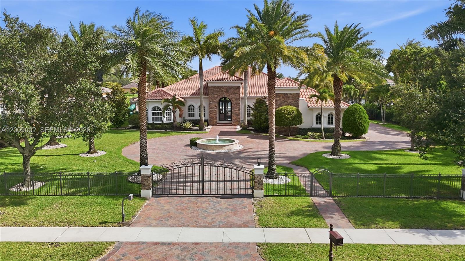 A one-of-a-kind single-story estate in prestigious Woodbridge Ranches with over 5,000 sq. ft. under air on nearly a full lakefront acre. It features 5 bed, 5 full baths, office/den, gym/media/game room, 4-car garage, impact windows and doors, abundant natural light, and soaring 12-foot ceilings. A grand arrival sets the tone with an expansive gated driveway, lighted custom fountain, side-loaded garage, and an 11-foot iron and glass entry door. Two full kitchens in the main house and pool house are appointed with high-end cabinetry, natural stone countertops, and premium Sub-Zero, Miele, and JennAir appliances. The attached pool house, with both a private entrance and direct access from the main house, includes an en-suite bedroom, spa-style bath with shower, freestanding Jacuzzi tub and separate cabana entrance, kitchen with Italian cabinetry, and open living area, ideal for guests, in-laws, or entertaining. The primary suite and two en-suite bedrooms feature large custom walk-in closets and spacious baths. Marble floors enhance the living areas and baths, bedrooms feature wood flooring, and the pool house has 24x48 porcelain tile. Designed for unforgettable outdoor living, it showcases sweeping lake views, a huge covered patio with summer kitchen, massive travertine deck, and heated pool with sun shelf and jetted spa. Further enhanced by 35 mature palm trees, landscape lighting, home automation, mosquito system, and 12-camera security system. There is no other home like it.