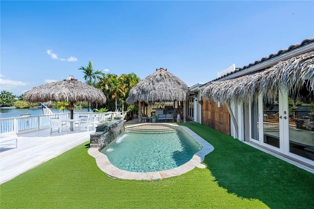 BIG PRICE DROP!!! HURRY NOW!!! Discover true lakefront living in this beautifully upgraded 5BR/3BA home. Elegant 24x24 marble floors flow throughout, with wood flooring in the office and full impact glass windows and doors. The updated kitchen features stainless steel appliances and a modern master bath. Step outside to your private paradise with a tiki hut, electric fans, outdoor kitchen, teak dining area, and teak accent walls. Enjoy the soothing sounds of a waterfall, paddleboard or fish from your floating dock, or relax on the sand beach entry to the lake. Additional highlights include a circular driveway and lush tropical landscaping. Located in a top-rated school district and walking distance to houses of worship, this home offers the perfect blend of beauty, comfort, and lifestyle.