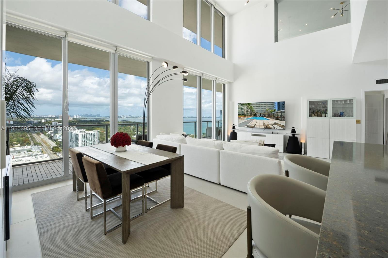 Turn the key to this fully renovated duplex penthouse at coveted 2Midtown, where soaring double-height ceilings, floor-to-ceiling glass, and a dramatic glass-enclosed den showcase sweeping Biscayne Bay views and exceptional natural light. PH102 offers 2,178 SF with 2 bedrooms + den, 2.5 baths, generous storage, and 500+ SF of private terraces for effortless indoor-outdoor living. Both levels are elevator-accessible. Two assigned parking spaces included.
Finished in refined contemporary style, the home features 36x36 porcelain floors downstairs, wide-plank wood-look porcelain upstairs, fresh paint, new baseboards, and polished concrete ceilings. The reimagined kitchen boasts custom cabinetry, a quartzite waterfall island, Bosch appliances, and LG washer/dryer. Both primary baths are fully renovated with floor-to-ceiling porcelain, frameless glass showers, custom vanities, and a new soaking tub upstairs. The powder room is refreshed with quartz and designer wallpaper. Additional upgrades include brass hardware, new lighting, solid wood doors, automatic blackout and sun shades, and a new A/C system.
2Midtown offers 24/7 concierge and security, a rooftop pool, resort-style spa facilities, fitness center, cabanas, playground, EV charging, and more — steps from the Design District, Wynwood, and Midtown's best dining and shopping.