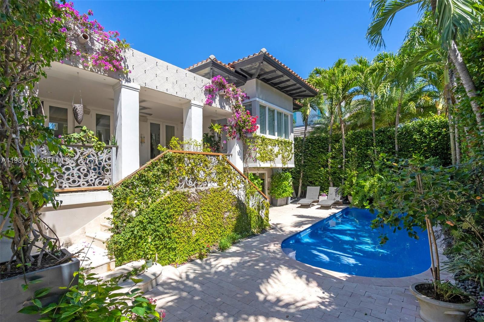 Elevated, 3,888 sf Adjusted Area. Sophisticated Mediterranean beach house, elevated and privately set, offering 5 bedrooms, 5 bathrooms, and an additional powder room, surrounded by a lush, mature backyard garden. A double-height cathedral ceiling in the great room fills the home with natural light and opens to a covered terrace overlooking the pool patio, creating seamless indoor-outdoor living. The great room flows into a warm family room and gourmet kitchen, well suited for everyday living and entertaining, and every bedroom is en suite. The serene primary suite includes a sitting area ideal for relaxing or reading.

A spacious den with abundant windows and its own full bath offers flexibility as a home office, guest suite, studio, or cabana, with direct access to the patio and pool. Outdoors, enjoy a private setting with an upper veranda shaded by a living canopy of fig vines, an inviting space for dining and lounging, plus an outdoor gourmet area with a wood-fired pizza oven and tools. Additional highlights include solar panels with backup batteries for energy savings and reliability. Two batteries plus potential for expansion, two garages, and a pool with refreshed tile and grout for a crisp, updated finish. Walking distance to the beach, parks, dining, shopping, and everyday conveniences, with convenient access to Miami. Not Included in the sale: all display shelving, two bronze candle holders, and the chandelier hanging above the stairs.