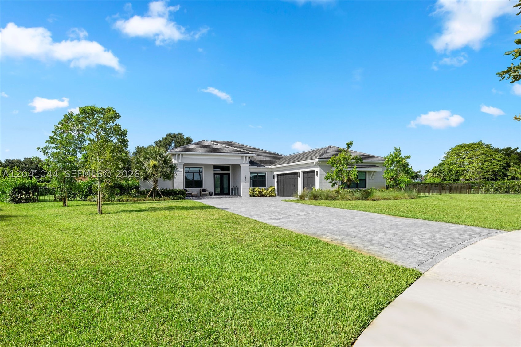 Set within Millstone Ranches, a private gated enclave of just 18 residences, this 2024 new-construction estate offers refined single-story living on nearly an acre of private, beautifully landscaped grounds. A thoughtfully designed split-bedroom plan separates a private owner's wing, complete with a dedicated office, from three secondary suites, each with its own walk-in closet and en-suite bath. Volume and tray ceilings, custom millwork, and designer lighting set a sophisticated tone, with polished large-format porcelain in the main living areas and warm wood-look porcelain in the bedrooms. The chef's kitchen anchors the open living areas with a premium JennAir appliance package, double wall ovens, gas cooktop, Calacatta Gold quartz, and an oversized waterfall island. The great room showcases a linear fireplace and custom built-ins, while the primary suite delivers dual walk-in closets and a spa-inspired bath with a freestanding soaking tub. Outdoors, a heated pool and spa with pre-plumbed connections for future water features take in serene lake views, set against a brick-paver deck, covered lanai, and mature privacy hedges. Engineered for South Florida living with impact glass, two Carrier HVAC systems, a three-car garage, 1,000-gallon propane, generator-ready infrastructure, an outdoor kitchen rough-in, and smart-home automation.