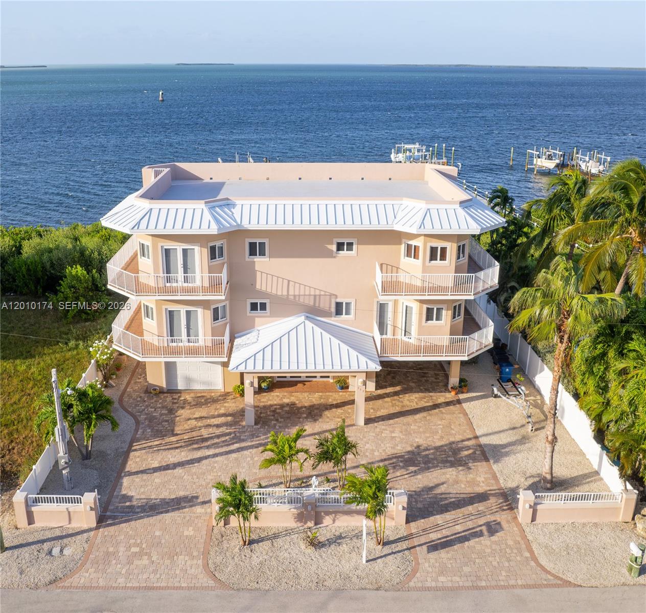 Experience luxury in the Florida Keys with this meticulously designed 5-bed, 5-bath, 4822sf home, ideal for large families. Spacious interiors, high ceilings, & 8ft doors. A private fenced yard features a heated pool and spa, ensures a relaxing retreat, enhanced by security cameras, two electric gates, and an intercom system.The grand foyer leads to stairs or an elevator. Main floor is an elegant living and dining area with ocean views. The kitchen, with a Benihana cooking station, top-tier appliances, and ample storage, connects to laundry room. 2 guest bedrooms with baths complete this level. 3rd floor hosts a master suite, his & hers walk-in closets, an office, media room with surround sound. 360-degree views from the rooftop. Boaters will appreciate the 225ft pier with a 25k boatlift.