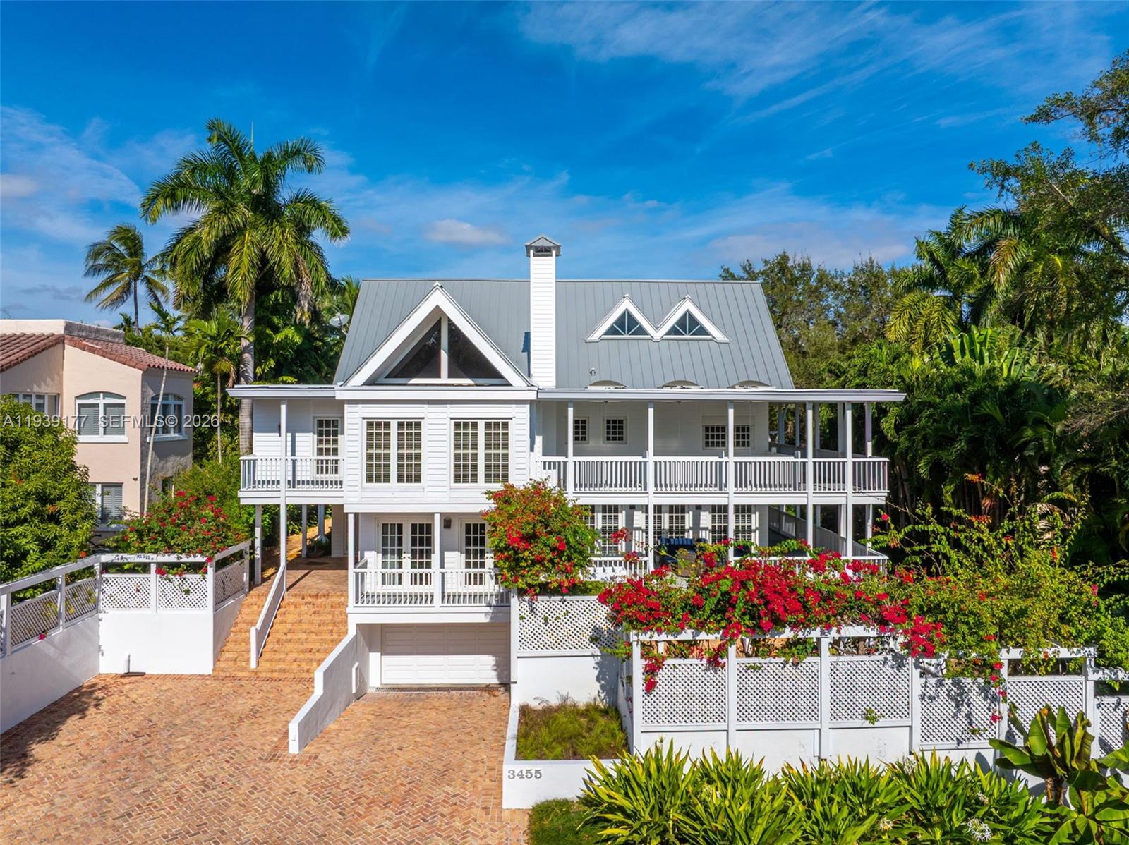 Perched on a natural ridge in the exclusive gated Moorings enclave, this 3-story classic Key West-style home is sited just 1 door in from the private community marina. Its premier location in the Grove’s most highly sought niche bayside neighborhood (only 42 homes where resident permission is required for entry!) makes this unique property all the more rare. Its coveted, walkable Main Hwy locale, just blocks from the Grove’s charming “downtown” village, enhances quality of life. The timeless Charles Harrison Pawley-designed residence features a new metal roof, new impact windows/doors, wraparound porches, volume ceilings, generously scaled interiors w/ oak floors & elevator. Its concrete construction is faced w/ resilient composition clapboard; its expansive covered porches offer gracious outdoor living across 2 floors; its formidable pedigree & great bones provide myriad options for simple refinements or curated updates. Floor 1: Formal living & dining rooms enjoy abundant natural light. Big, bright, beautiful eat-in kitchen. Floor 2: Exceptional vaulted primary suite appointed w/ His & Hers baths & walk-ins; 3 additional bedrooms; full laundry. Floor 3: Architecturally distinctive flexible space appointed w/ office & gym-easily converted to playroom, studio etc. Ground Level: 4/6-car capacity garage, full bath & vast storage that could be reimagined.
Chicago brick patios & paths frame the mature tropical landscape. Peerless location, timeless design, unlimited potential.
