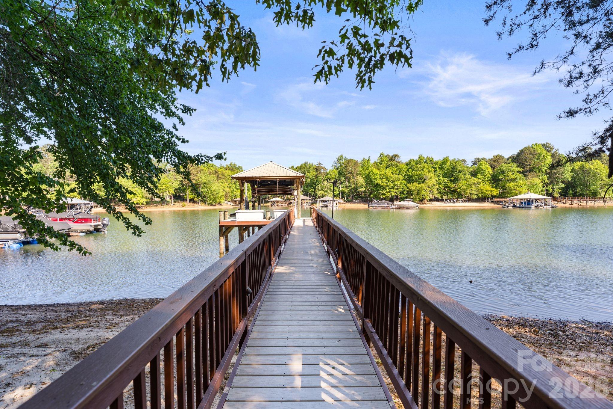 Experience elevated lakefront living in Denver’s premier Sailview community! Situated on an exclusive lot with 76 feet of private shoreline, this exceptional waterfront property features a deep-water pier designed for both convenience and entertainment. The composite-decked dock includes a fixed pier, boat lift, WiFi access, Sonos sound system, motorized automatic touchless boat cover with remote, and remote-powered jet ski lift, everything you need for effortless days on the water. Enjoy your own private sandy beach and firepit, the perfect setting for sunset gatherings by the water. The backyard is a true entertainer’s retreat with a stunning two-level terrace highlighted by a new patio (2019), composite decking, and a dramatic double-sided stone fireplace. Relax year-round in the Bull Frog A9 spa, enjoy two gas heaters for cooler evenings, and take advantage of the outdoor shower after lake days. Additional exterior features include in-ground irrigation pumped directly from the lake, a 10x10 storage shed, landscape lighting, and a tranquil water fountain. The extended private driveway creates an impressive approach to the home while enhancing privacy, and the additional parking pad offers convenient space for extra vehicles, entertaining, or everyday flexibility.  Inside, a soaring 19-foot foyer ceiling makes an unforgettable first impression, with 12-foot ceilings throughout the dining and living rooms enhancing the open, airy feel. Hardwood floors were refinished in 2019 with a rich walnut stain. The kitchen showcases painted cabinetry and island, granite countertops, KitchenAid appliances, and a sunny breakfast nook framed by a wall of windows overlooking the lake. The great room features a gas log fireplace with custom built-ins, while a beautifully appointed sunroom (completed in 2019) offers a floor-to-ceiling stone fireplace topped with a reclaimed wood mantel. The main level also includes a secondary bedroom with full bath and a spacious laundry room with cabinetry and ample storage. Upstairs, the primary suite provides a private retreat alongside two additional bedrooms and an expansive bonus room with built-in desks, custom bench seating, and durable vinyl plank flooring. The finished basement expands the living space with an office or fifth bedroom, full bath, kitchenette, sitting room, recreation area with included pool table, media room, and abundant storage. Residents of Sailview enjoy access to a community pool, pickleball and tennis courts, clubhouse, and year-round social event, offering not just a home, but a lifestyle.